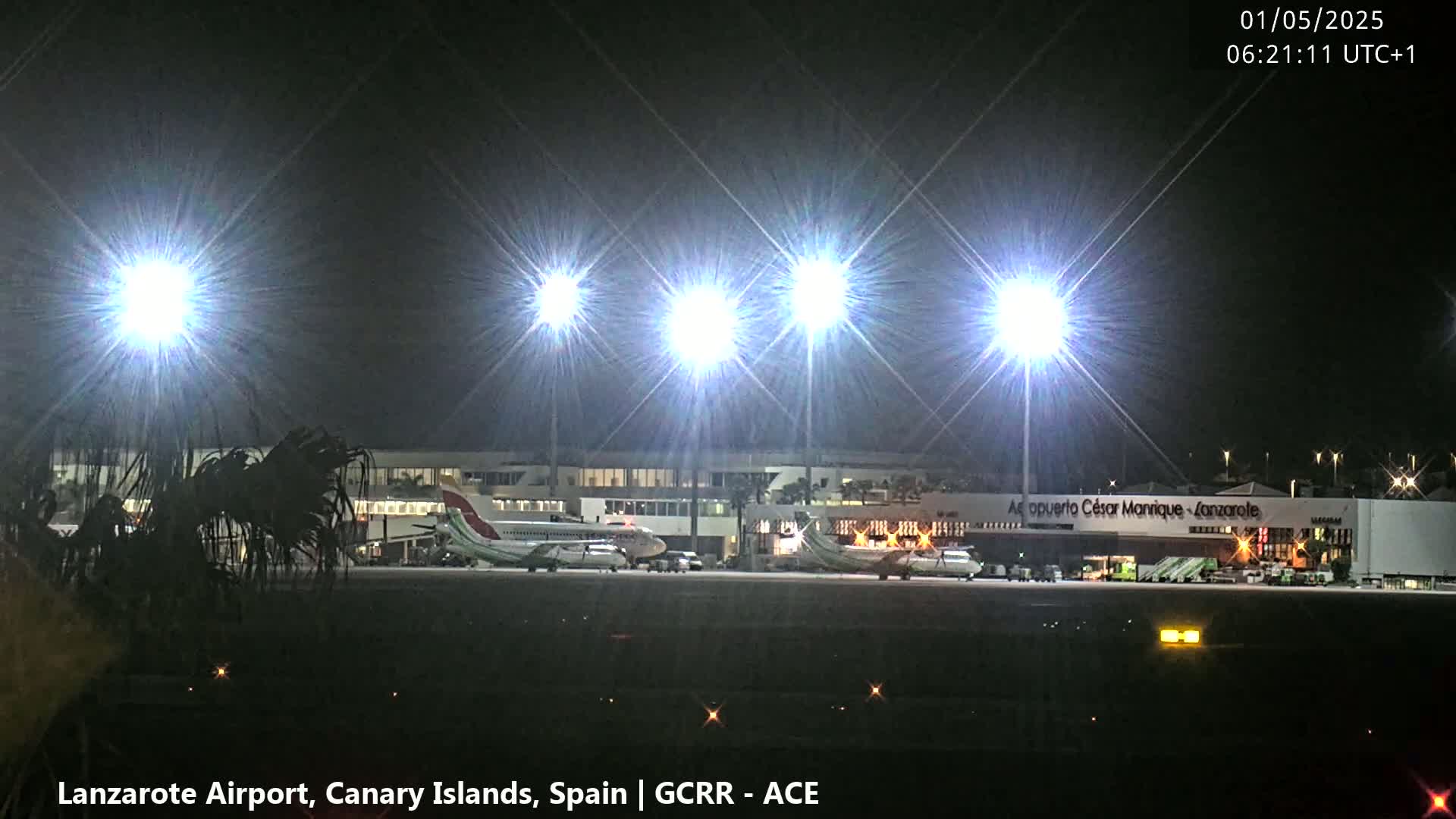 At night, brightly lit airplanes are parked at an airport terminal under a clear, dark sky.