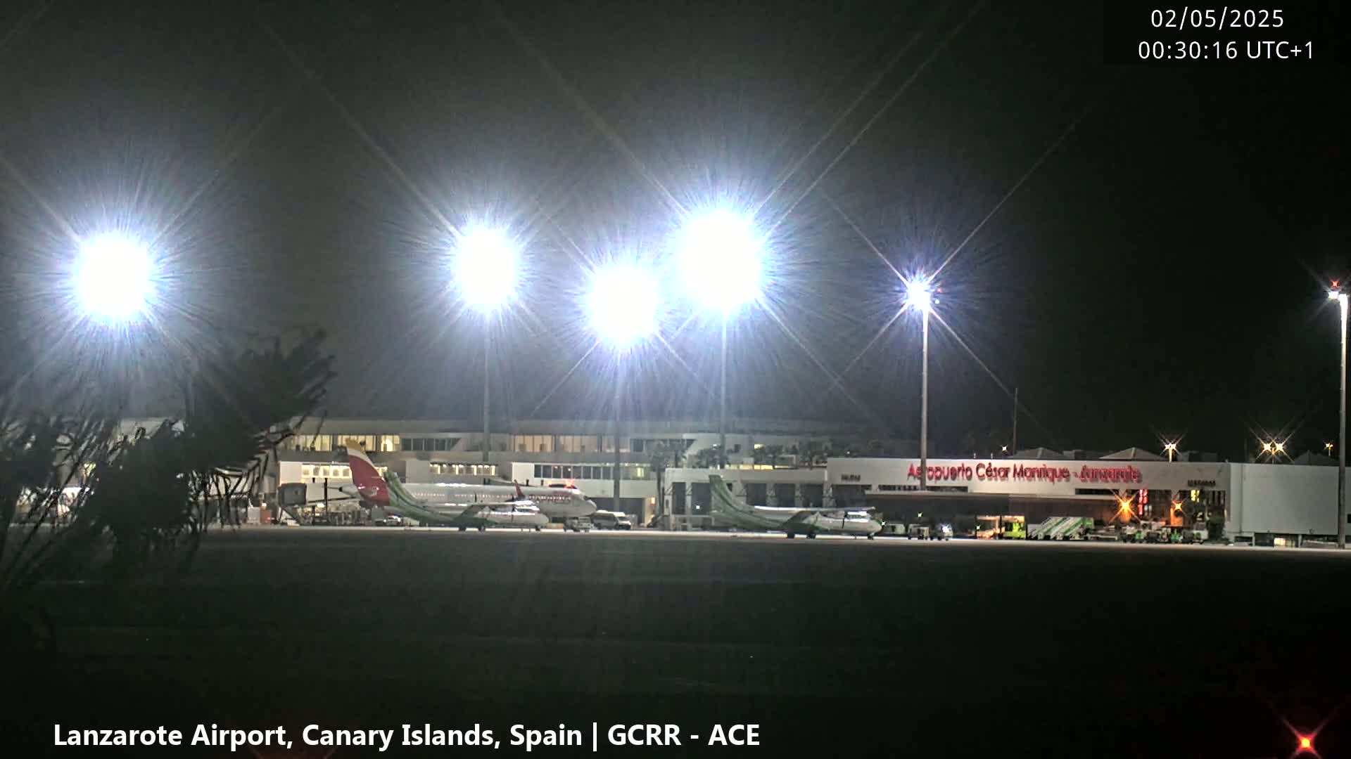 At night, several airplanes are parked on a brightly lit airport tarmac.