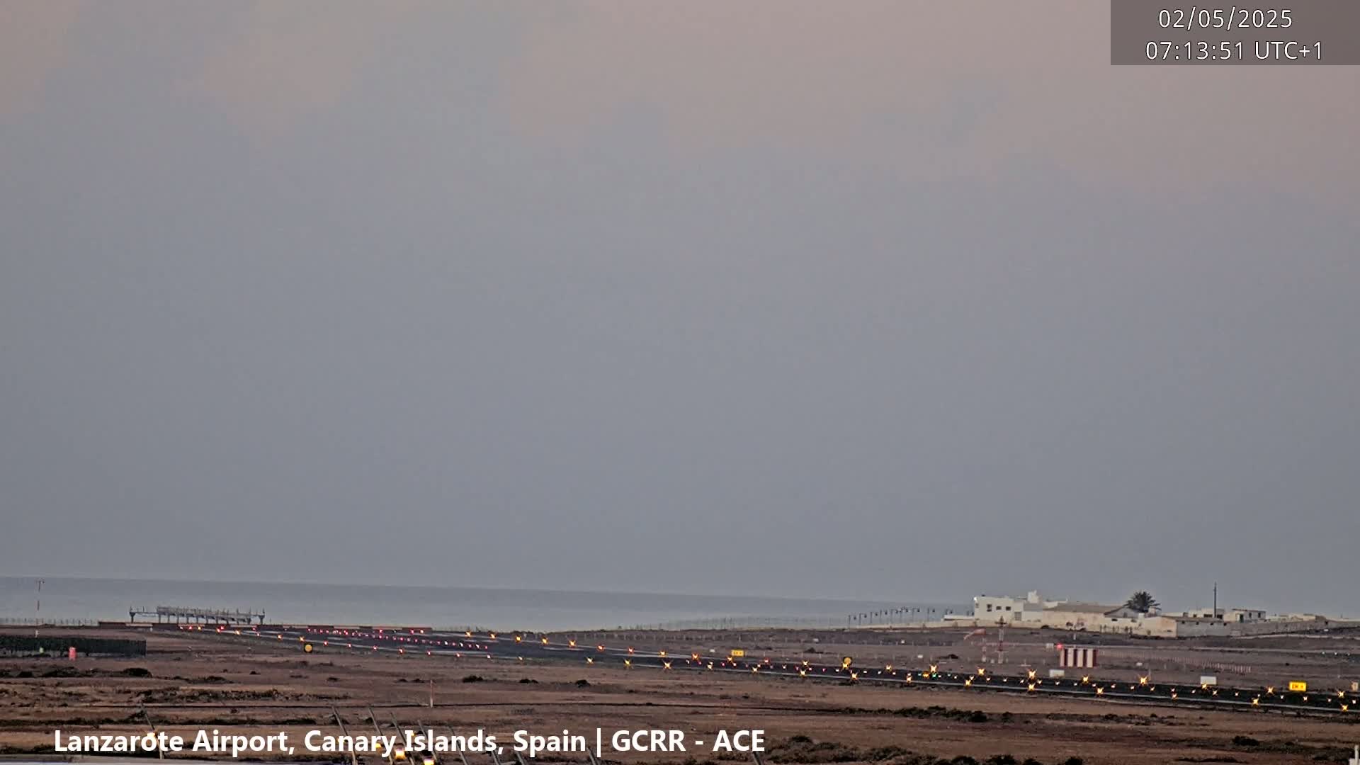 A long runway at an airport near the ocean is visible under a cloudy, overcast sky.