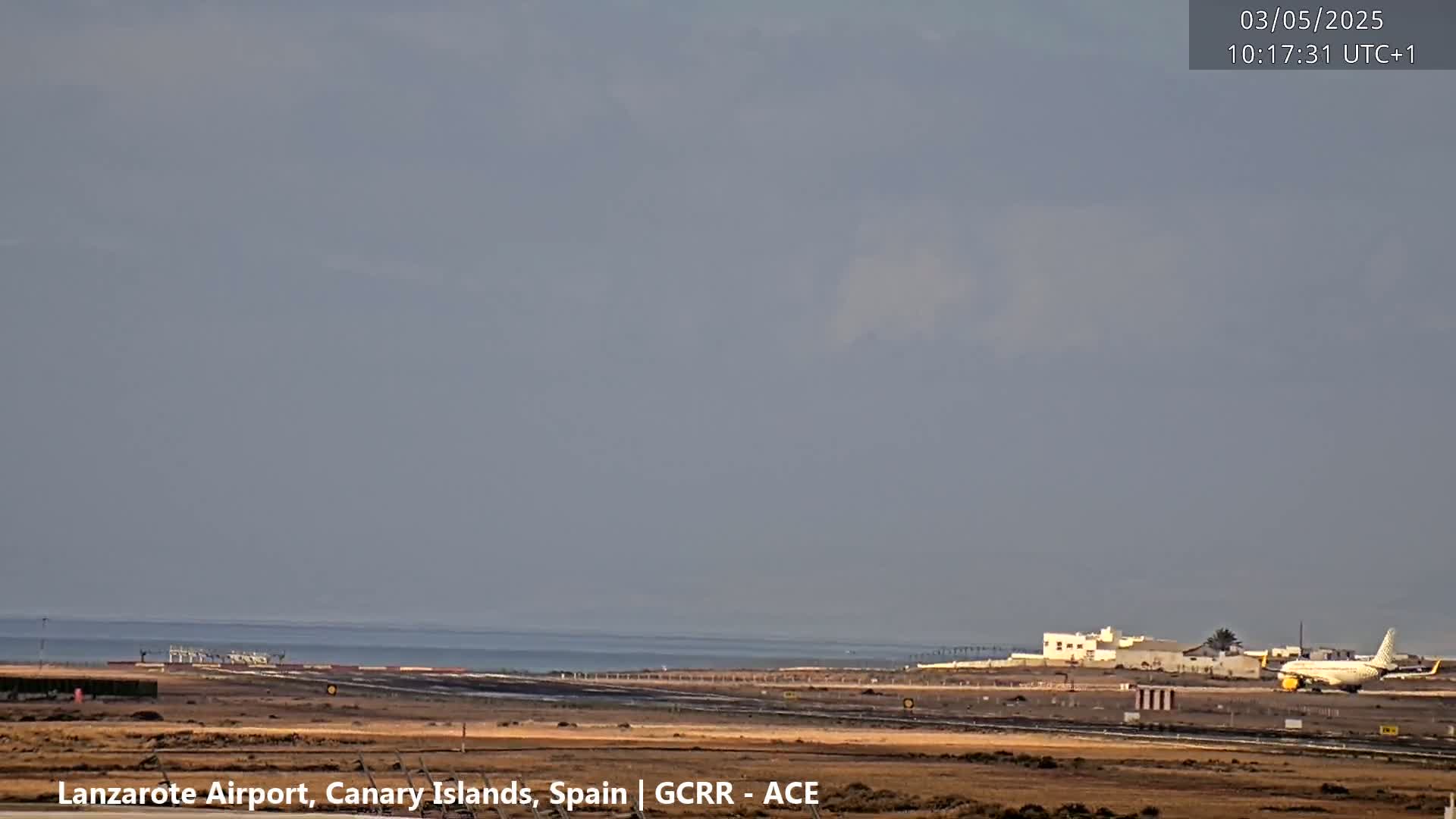 An airplane is taxiing on a runway near an ocean under an overcast sky.