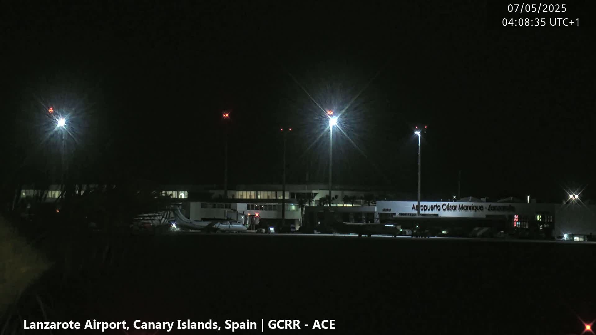 A nighttime view of an airport terminal with several brightly lit lights illuminating the tarmac and surrounding area under a clear, dark sky.