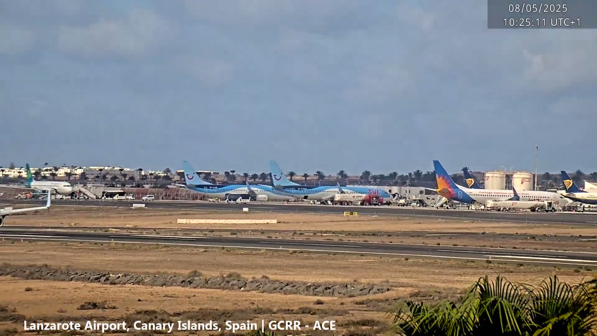 Several airplanes are parked at an airport tarmac under a mostly clear sky.