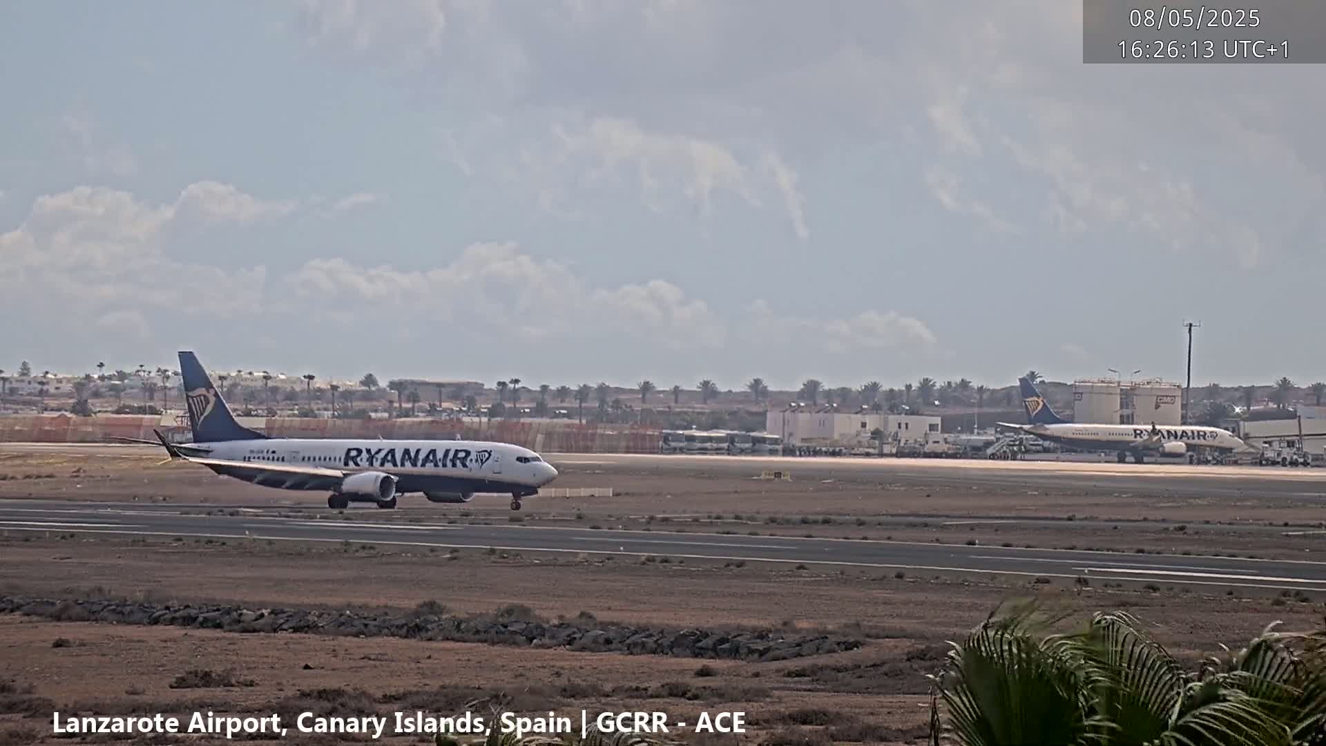 Two Ryanair airplanes are on an airport tarmac under a partly cloudy sky.