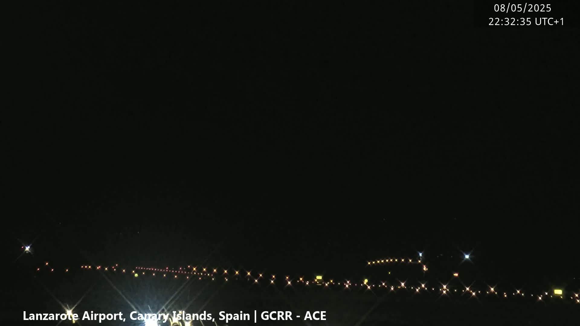 A nighttime view of an airport runway with lights illuminating the tarmac under a clear, dark sky.