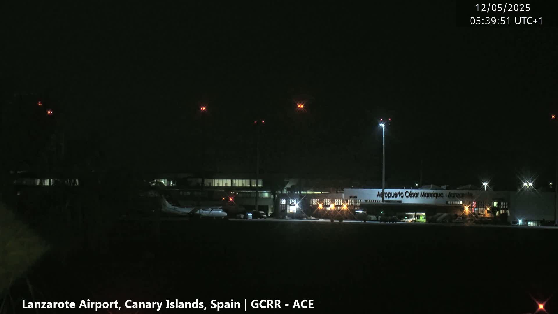 At night, airport buildings and airplanes are dimly lit on a tarmac under a dark sky.