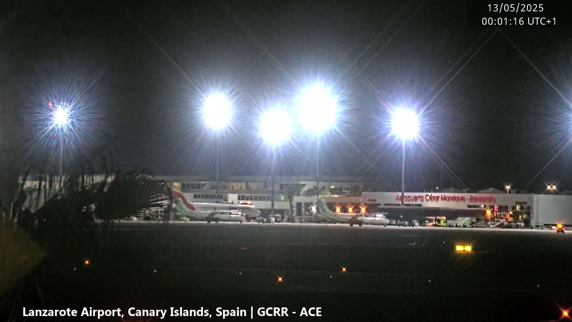 At night, brightly lit airplanes are parked at an airport terminal under several intensely bright lights.