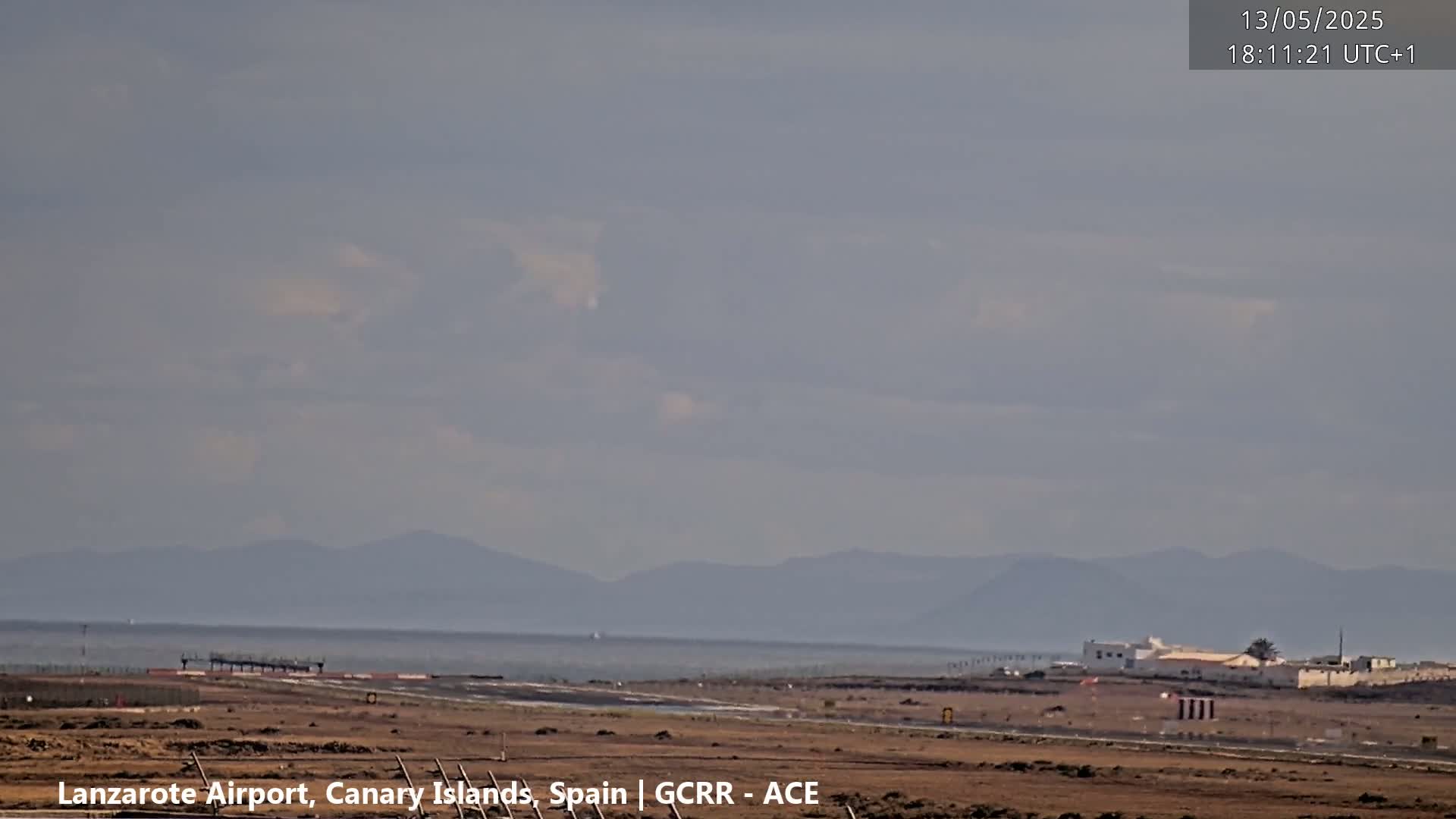 A long shot of an airport runway and terminal building on a hazy day with mountains visible in the distance.