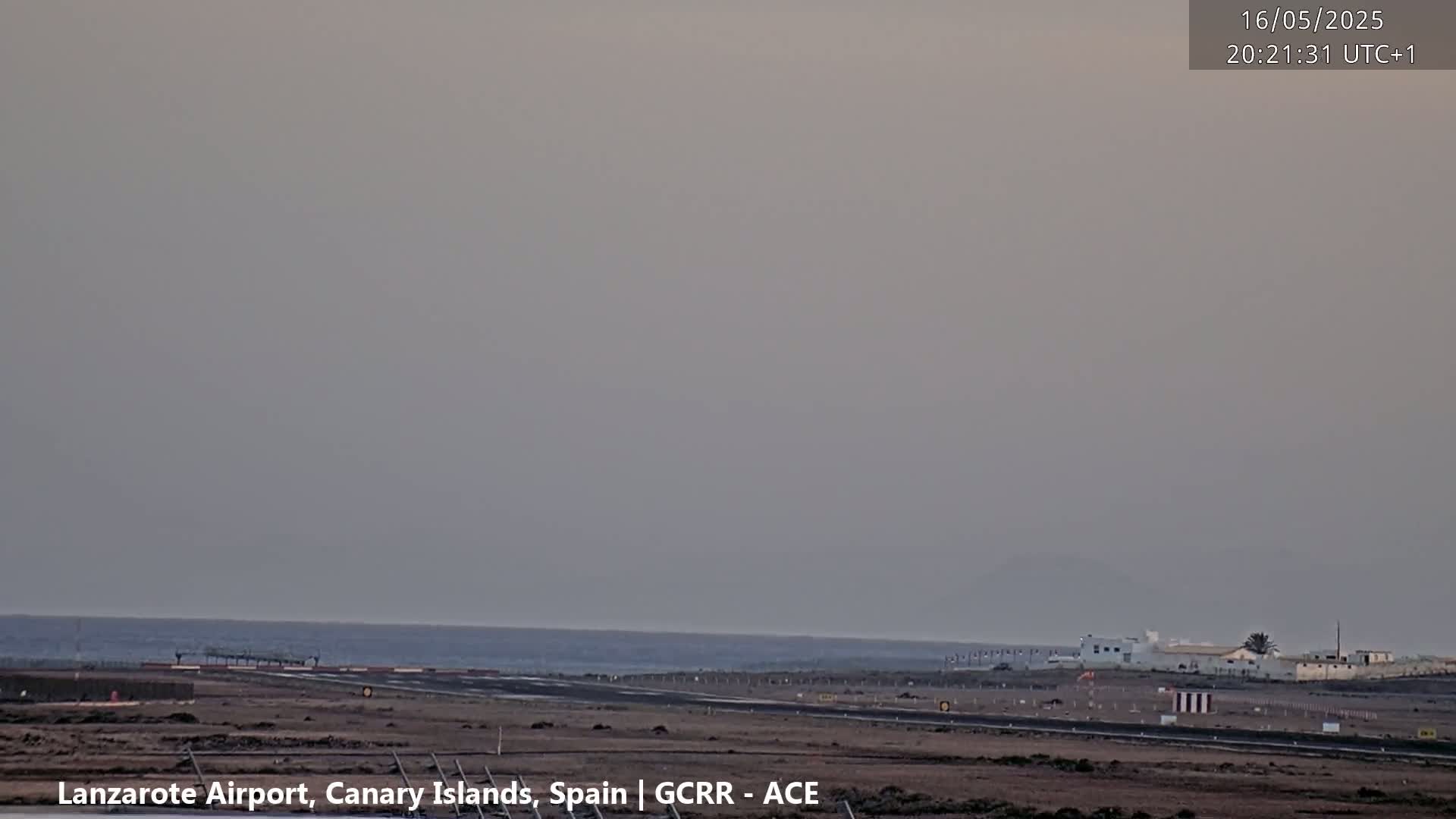 A hazy view of an airport runway next to the ocean under a muted sky.