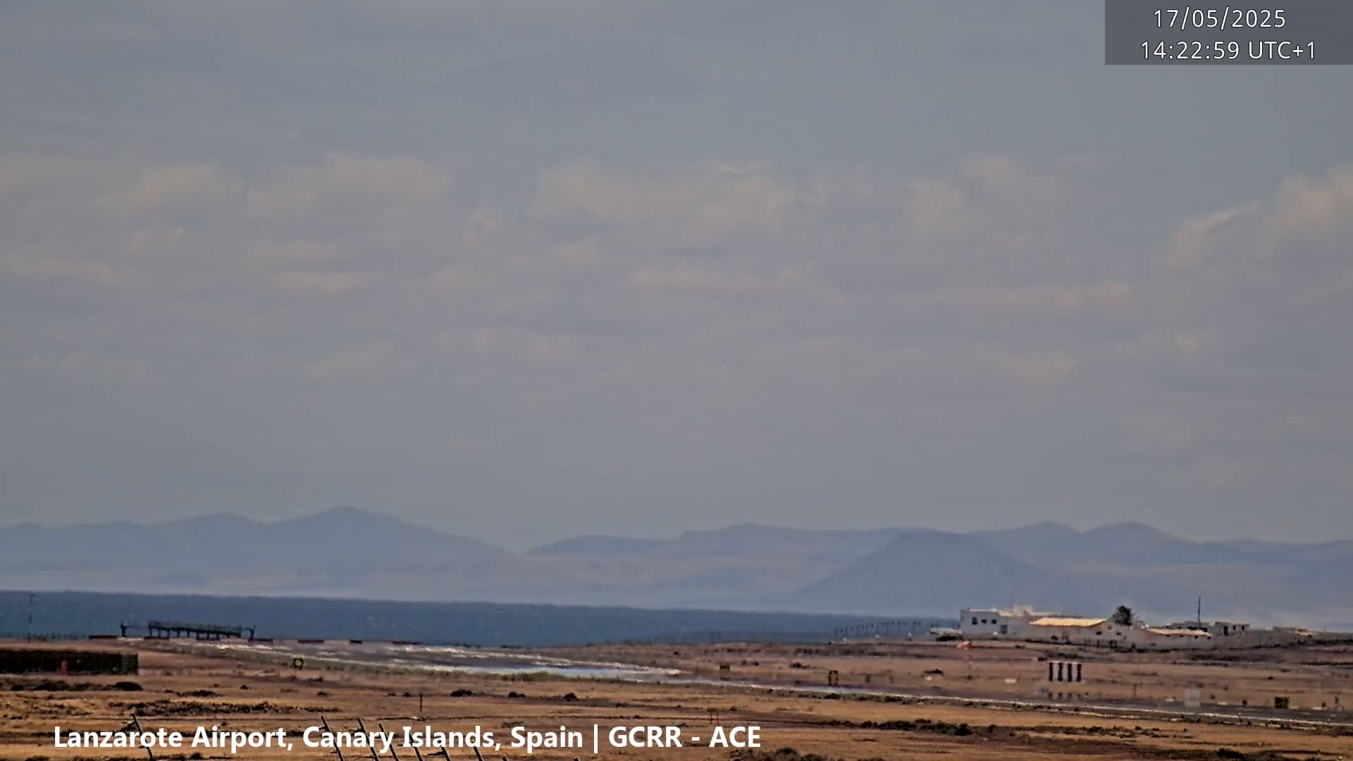 A mostly cloudy sky over a flat, arid landscape with distant mountains and a runway.