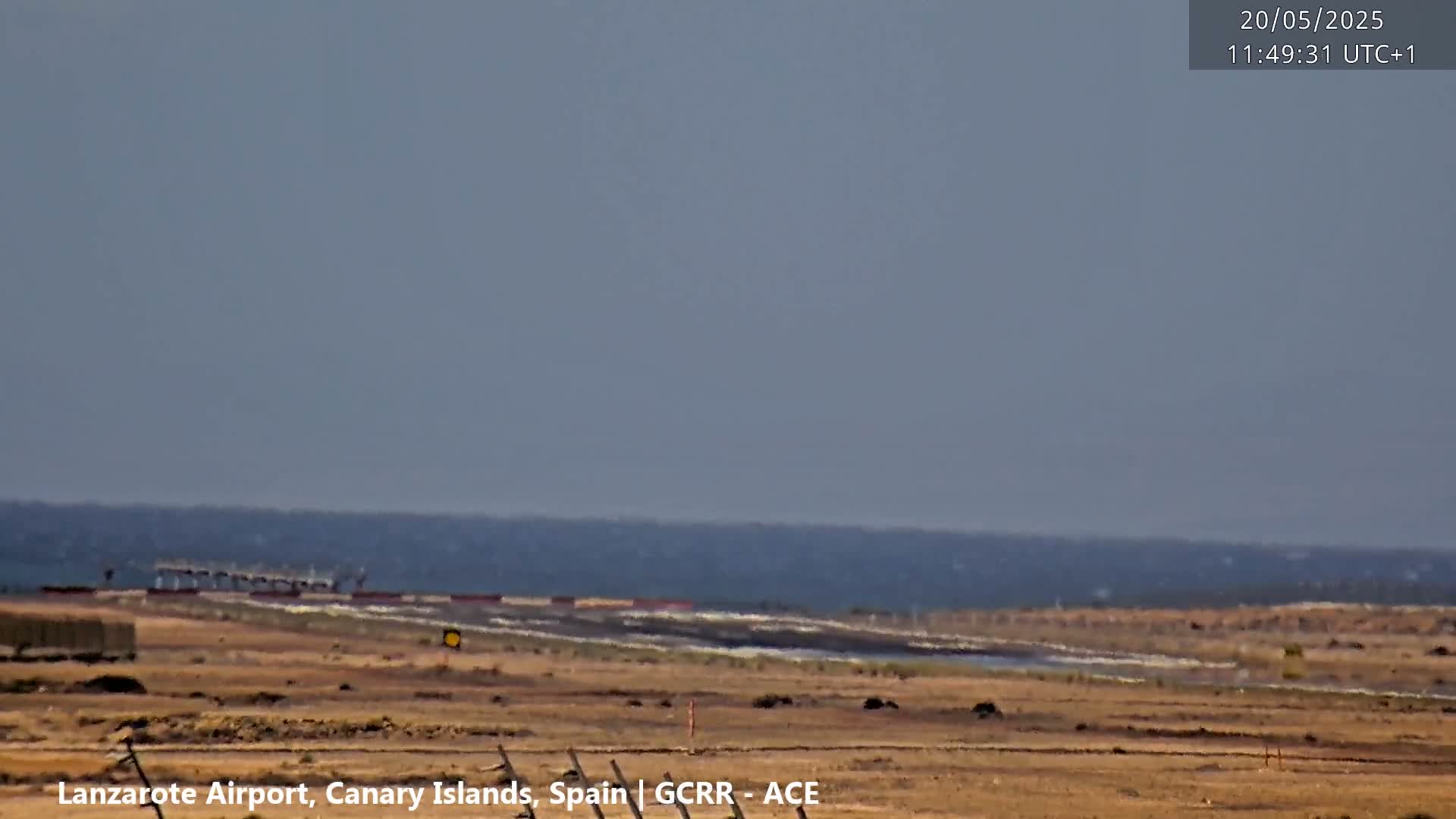 A long shot of an airport runway and a calm ocean under a hazy sky.