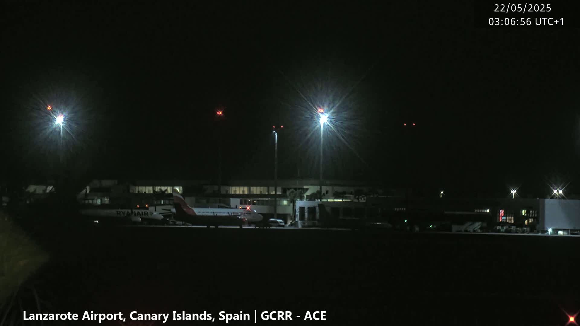 At night, a Ryanair airplane sits on the tarmac of an airport illuminated by bright lights.