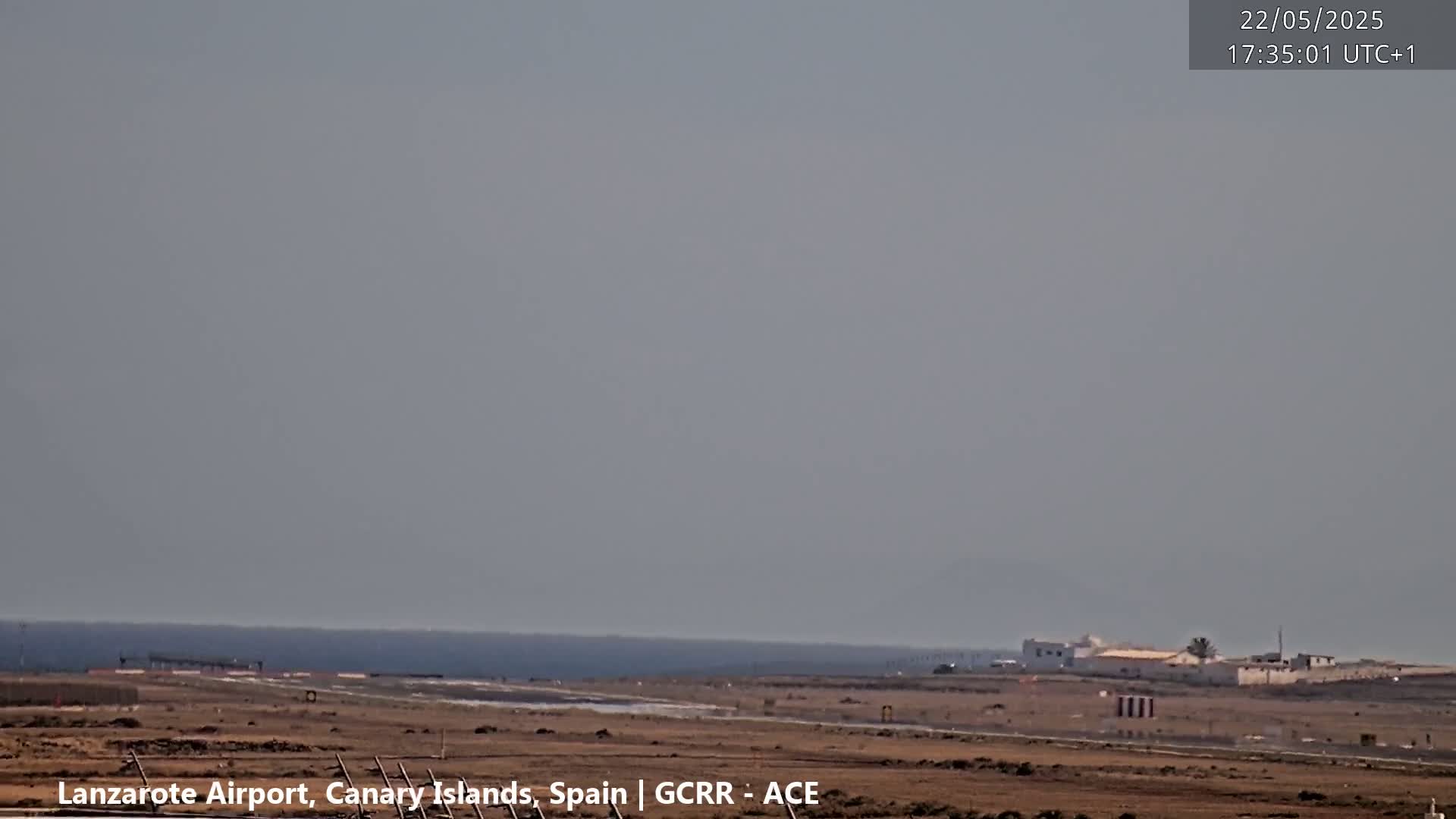 A hazy, daytime view of an airport runway with a calm ocean in the background.