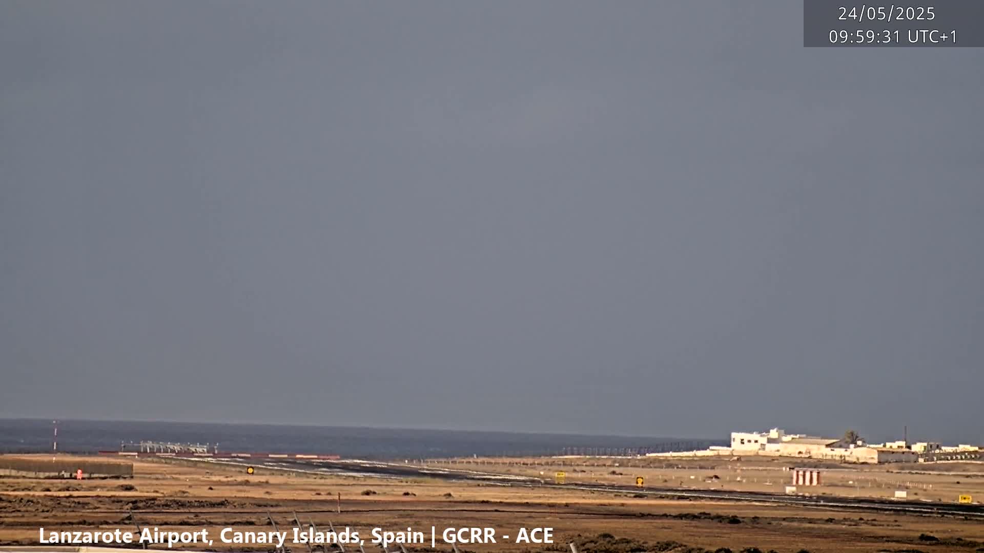 A mostly cloudy sky overlooks an airport runway adjacent to a calm ocean.