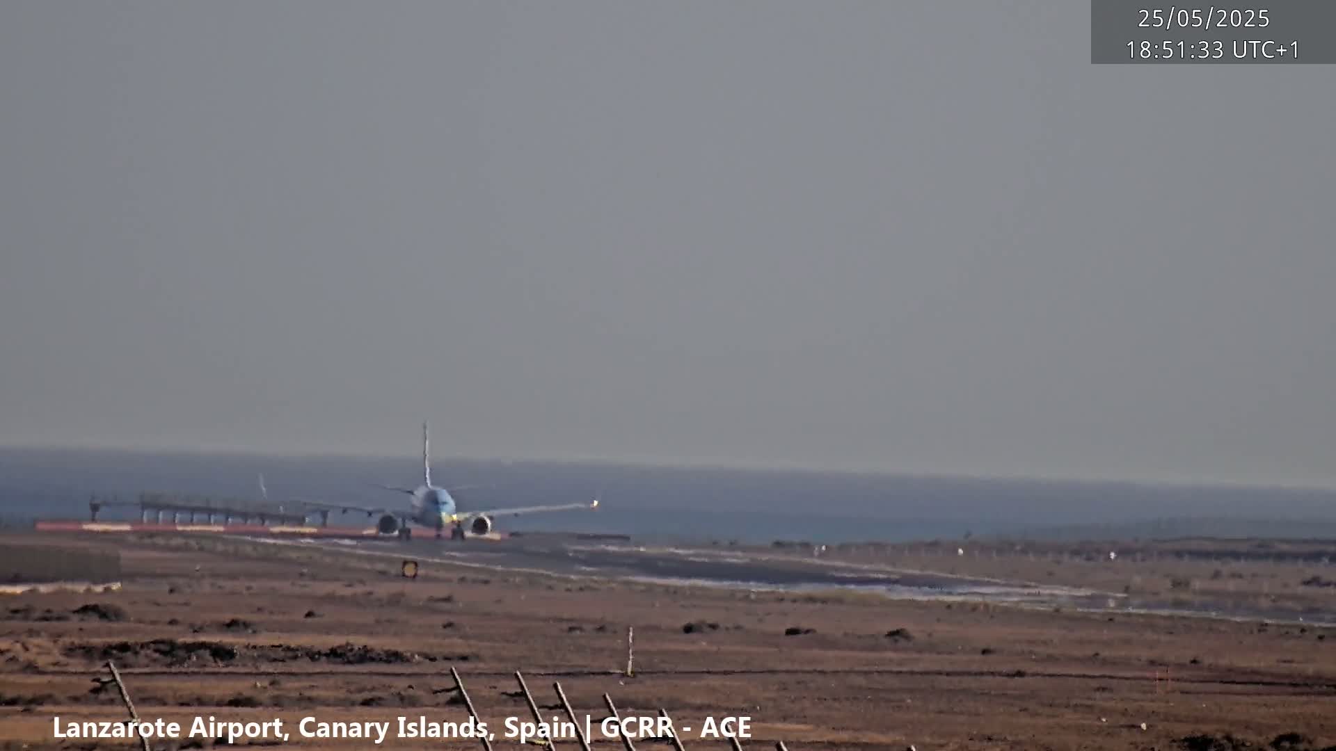 A passenger airplane taxis on a runway near a calm ocean under an overcast sky.