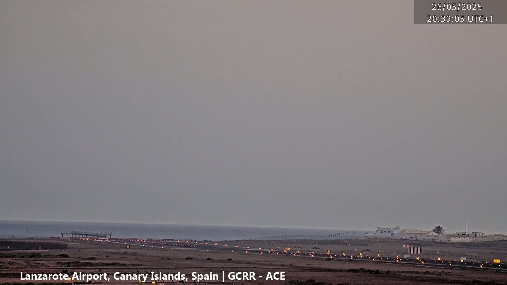 A hazy, twilight view of an airport runway extending towards a calm ocean.