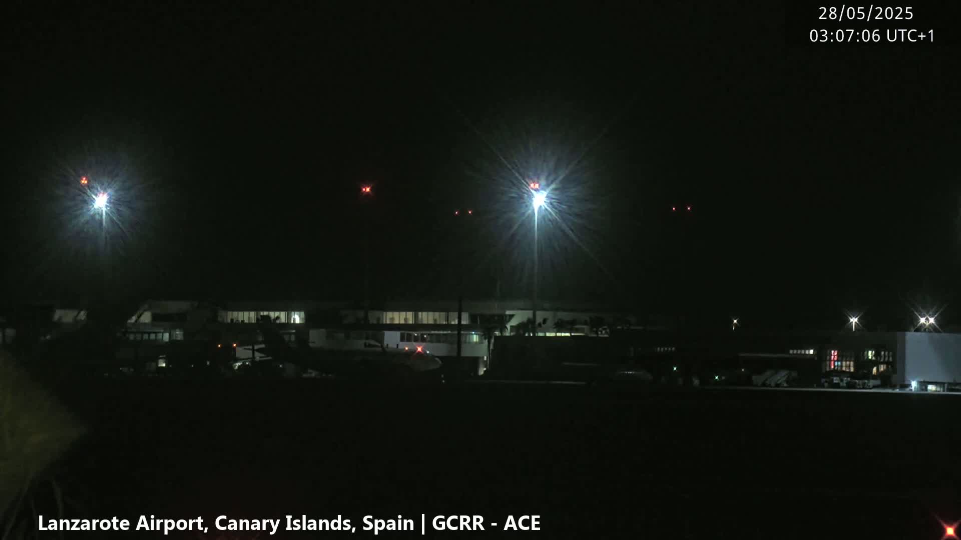 At night, brightly lit airport buildings and runways are visible under a dark, clear sky.