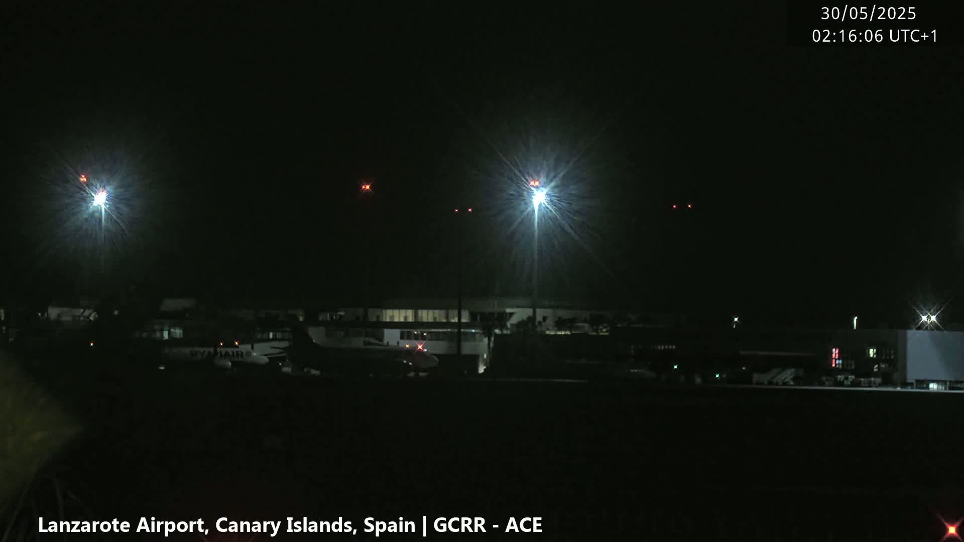 At night, brightly lit airport grounds show several airplanes parked near a terminal building under a clear, dark sky.