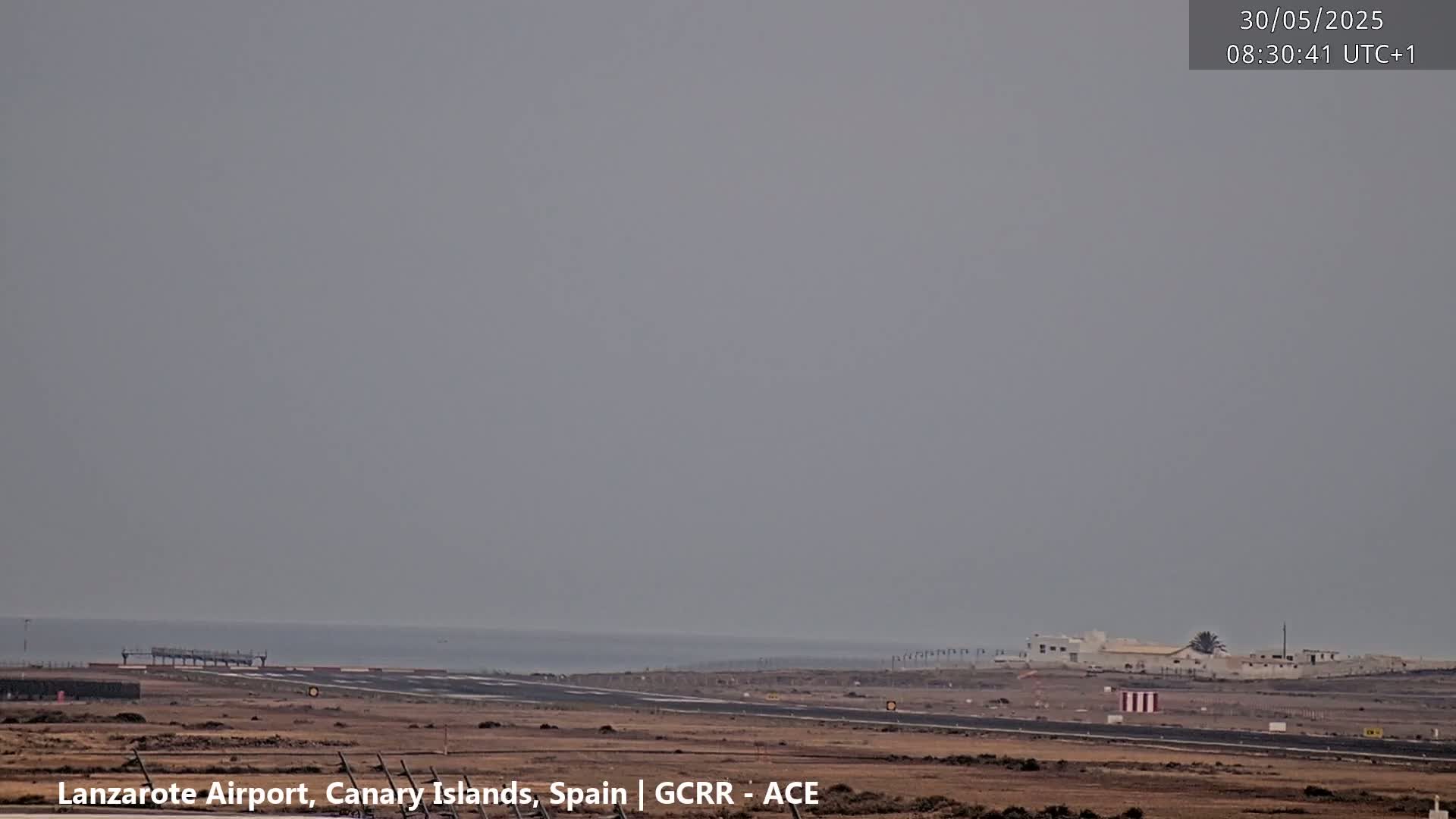 A hazy, overcast view of an airport runway and a calm ocean in the distance.