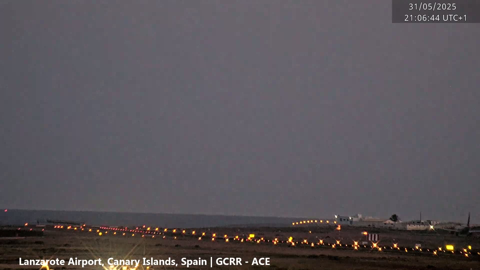 A dark, overcast sky over a lit-up airport runway at night next to the ocean.