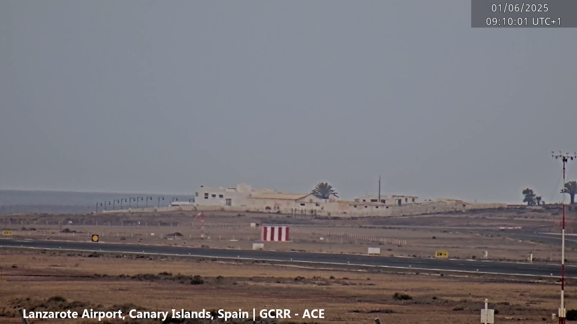 A long shot of an airport runway and buildings on a hazy day with a calm ocean in the background.