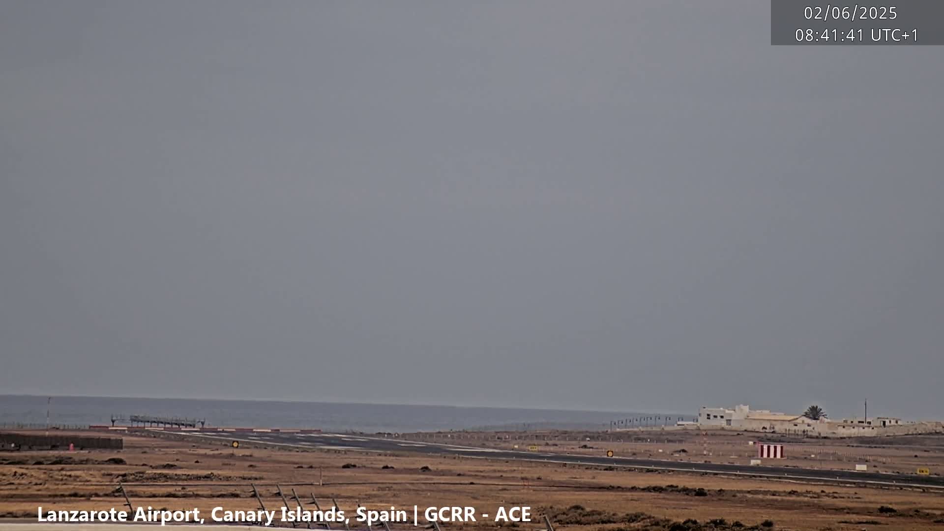 A long shot of an airport runway extending to a calm ocean under an overcast sky.