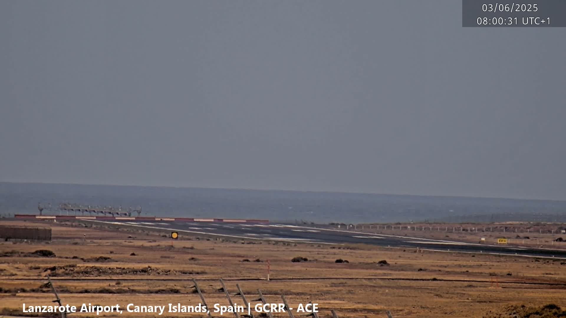 A hazy, distant ocean view is seen beyond a runway at an airport.