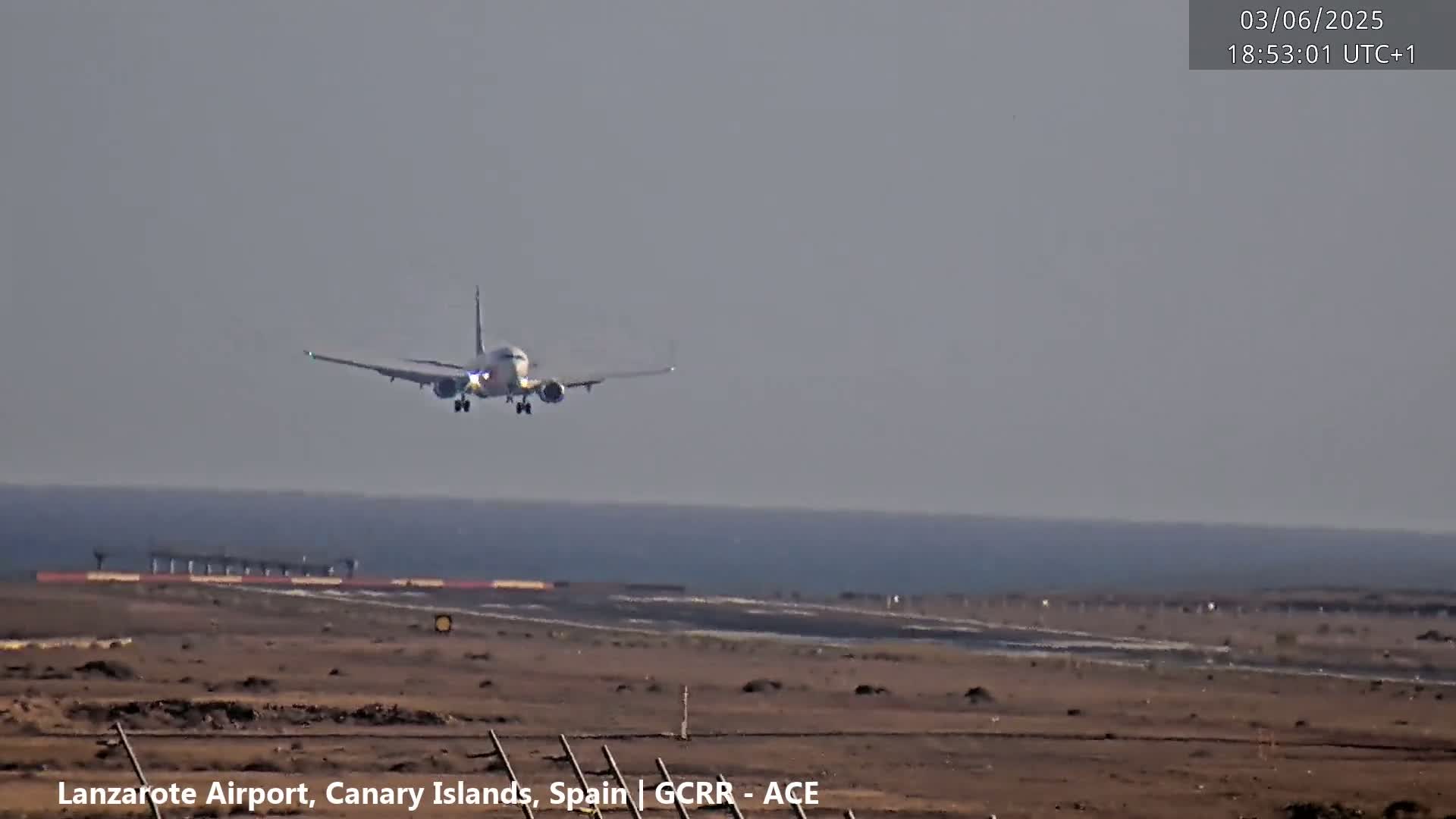 A large passenger airplane is in the process of landing on a runway near a body of water under hazy skies.
