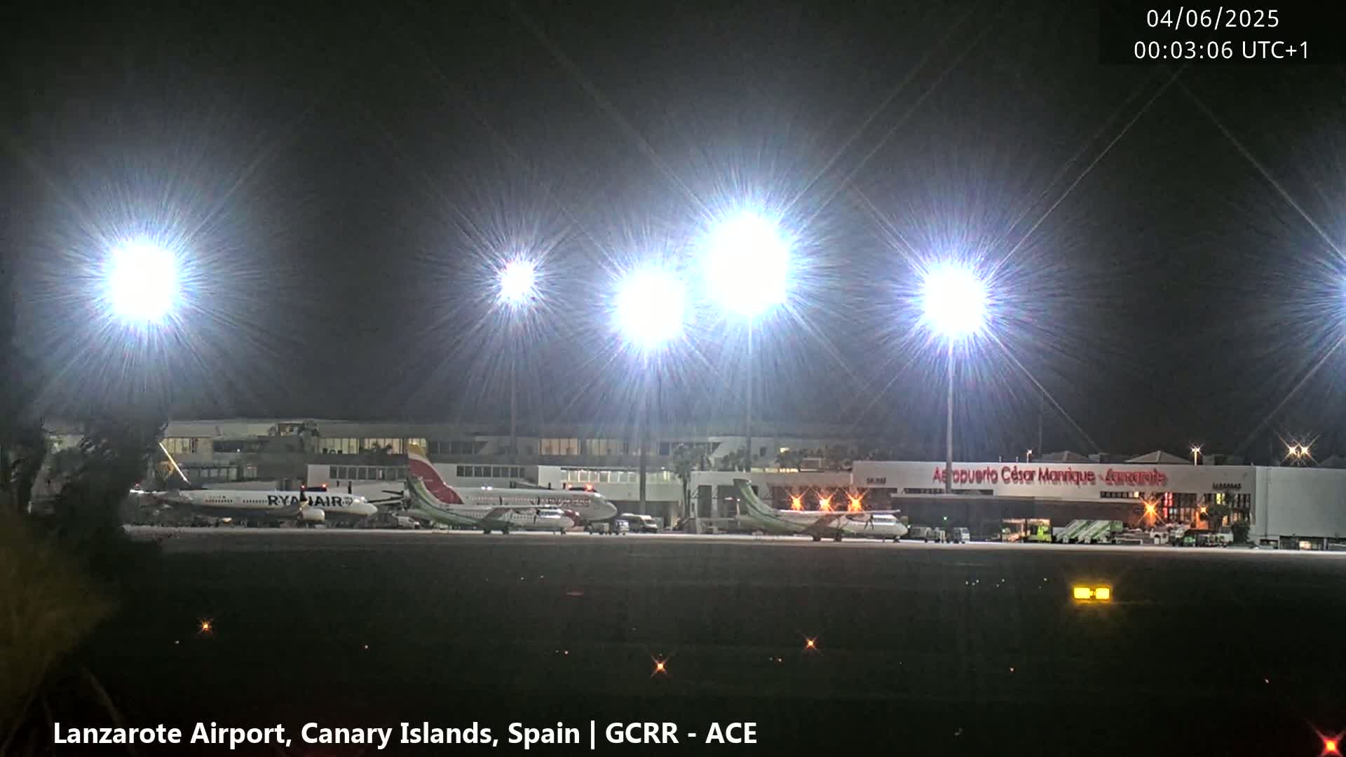 Several airplanes are parked at a brightly lit airport at night.