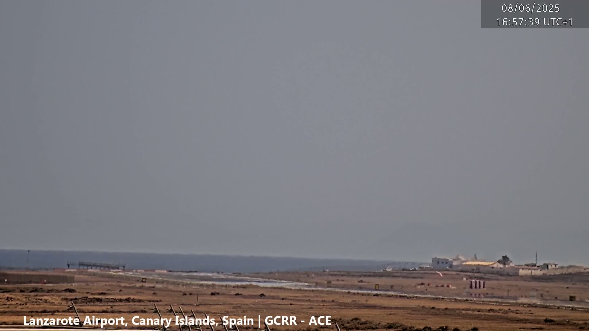 A hazy, overcast day shows an airport runway extending toward a calm ocean.
