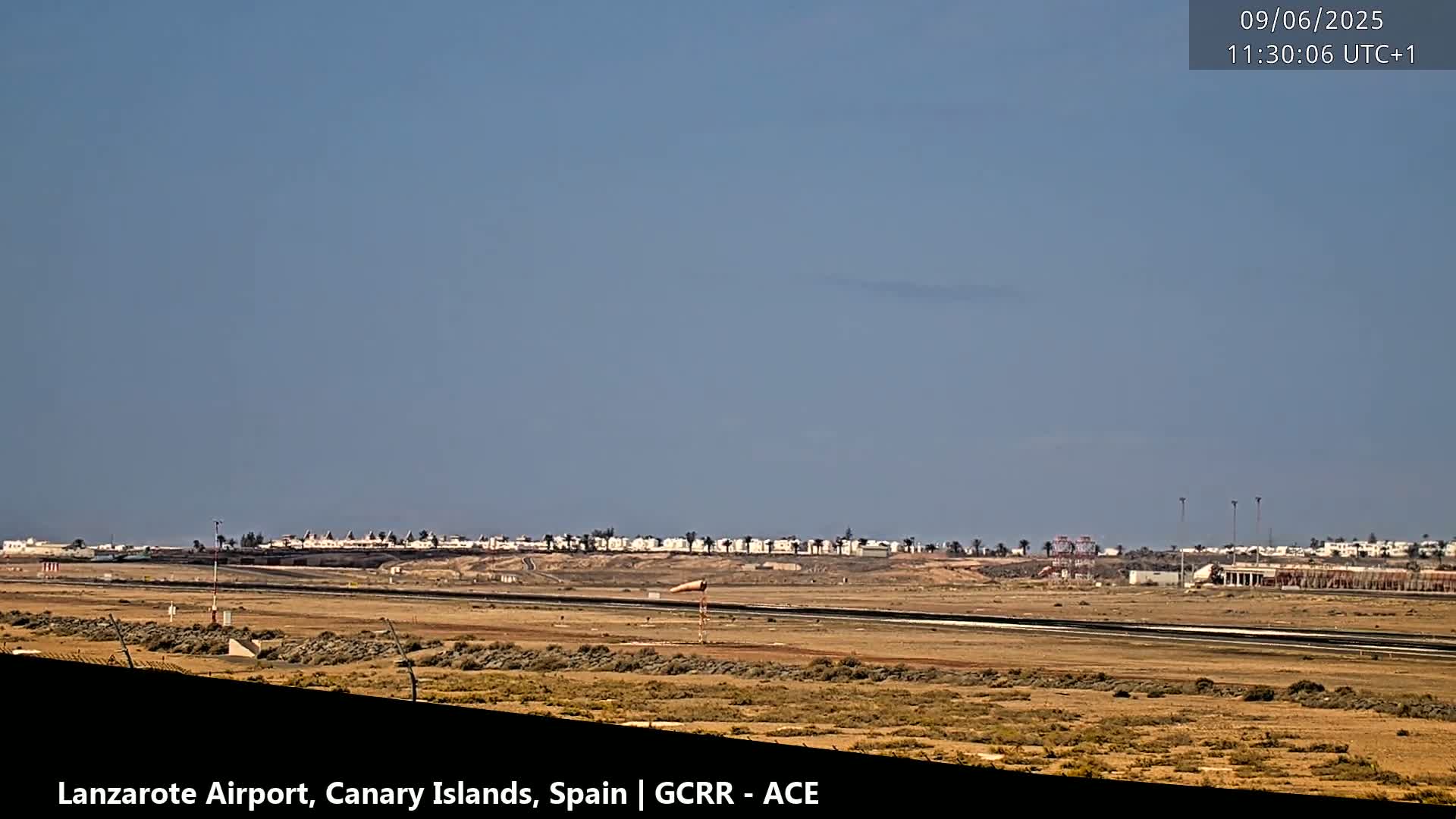 A long shot of an airport runway and surrounding buildings under a clear, bright sky.
