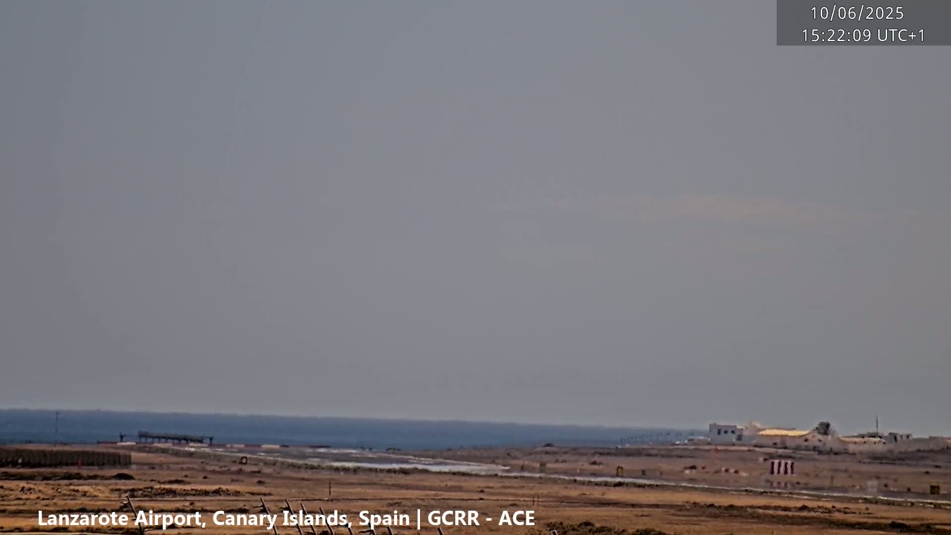 A hazy, overcast day reveals a coastal landscape with a body of water, flat land, and a few structures in the distance.