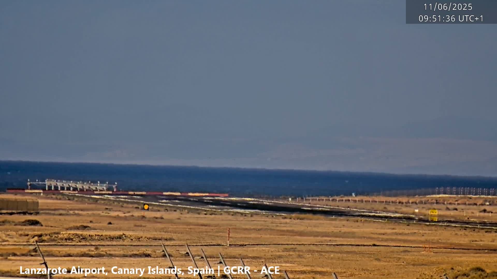 A long shot of an airport runway and surrounding arid landscape under a hazy sky.