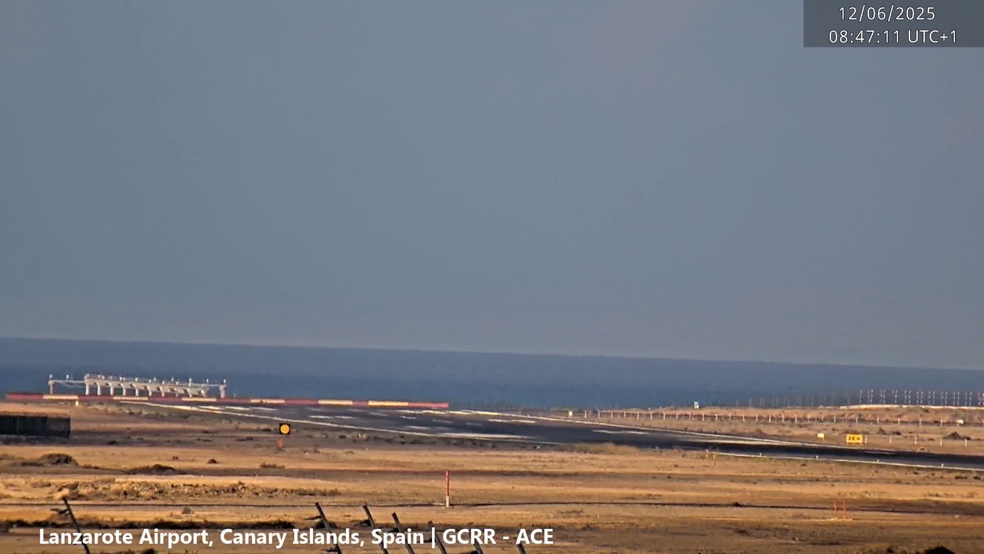 An airport runway is visible, extending towards a calm ocean under a clear, light-grey sky.