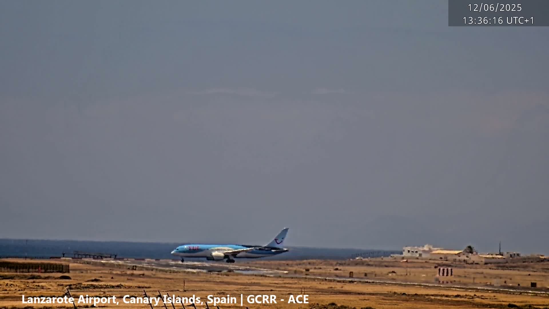 A large passenger airplane is landing on a runway near a calm ocean under a hazy sky.