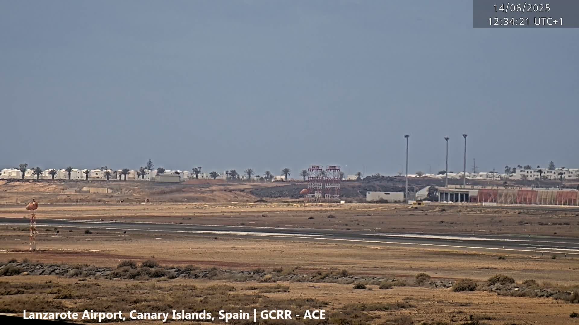 A mostly clear, dry day reveals an airport runway, surrounding buildings, and distant low-lying structures.