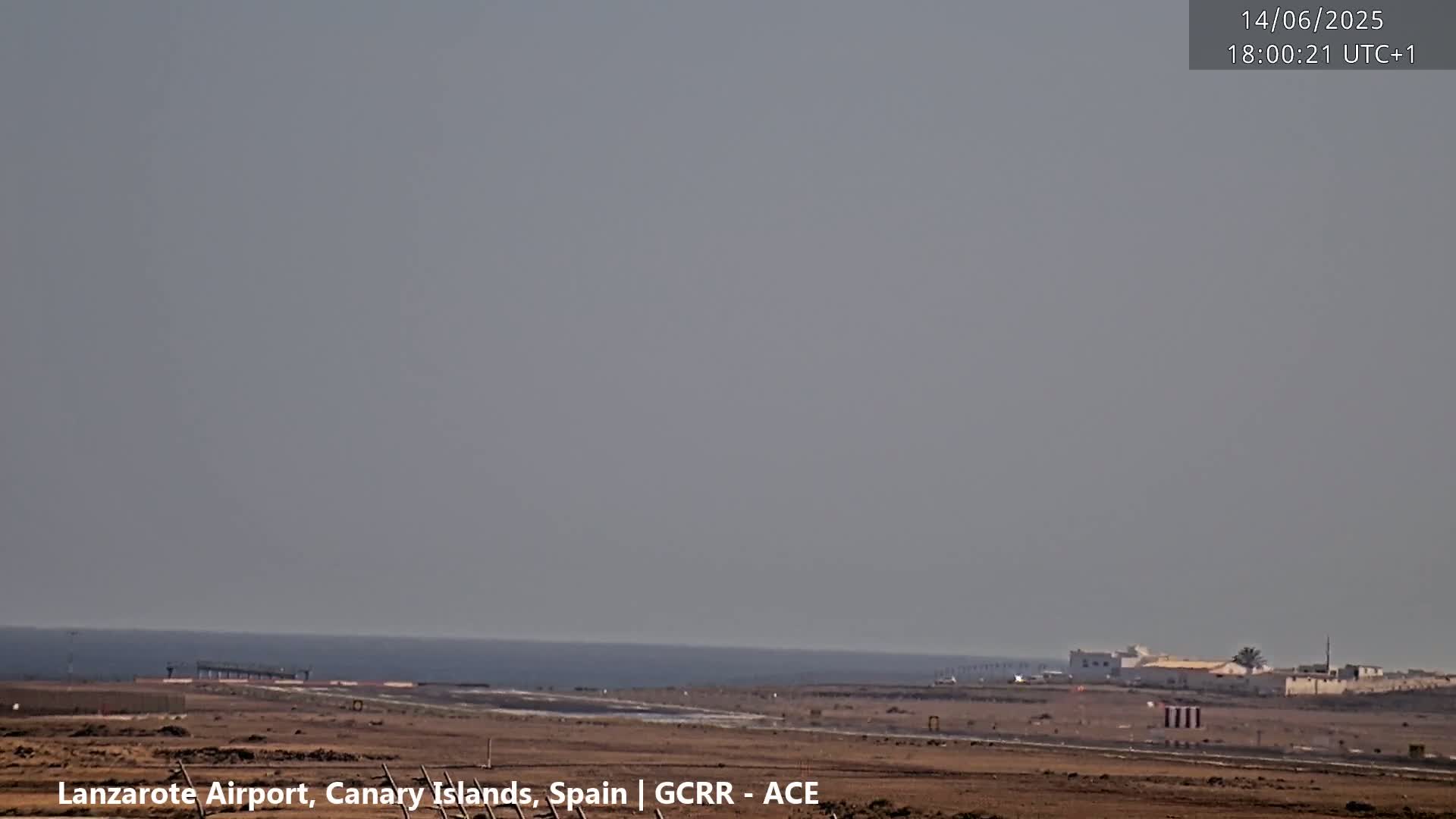 A hazy, overcast day shows an airport runway with a calm ocean in the background.