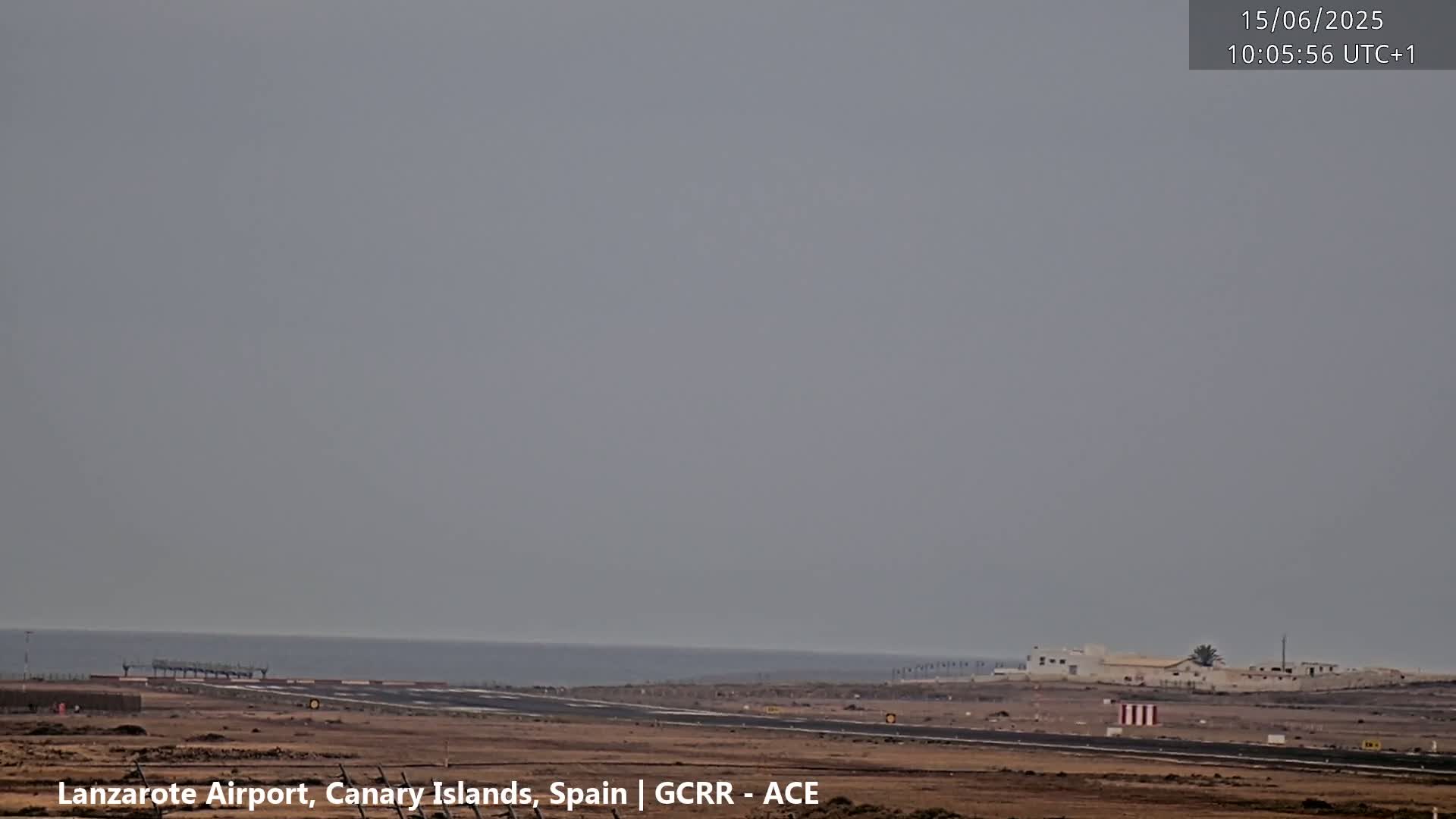 A hazy, overcast sky overlooks an airport runway next to a calm ocean.