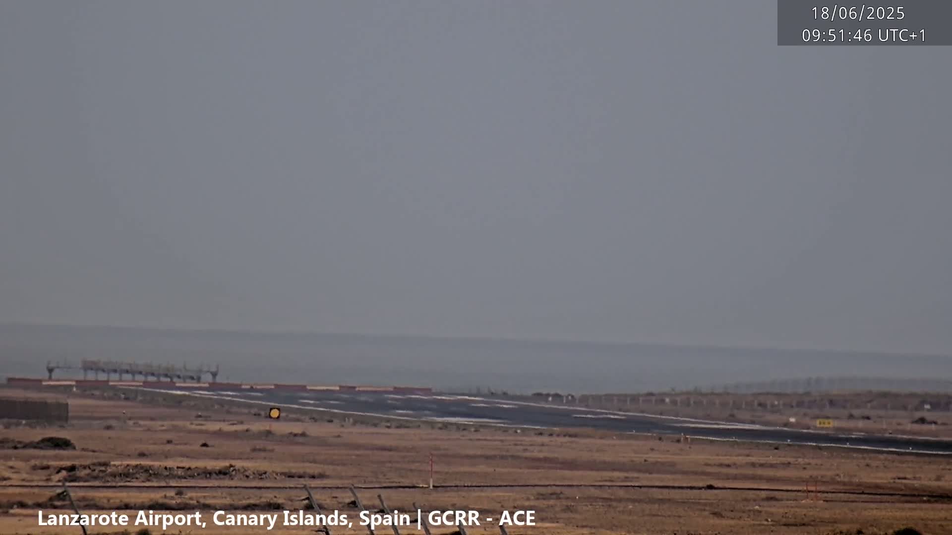 A hazy view shows an airport runway stretching toward a calm ocean under a gray sky.
