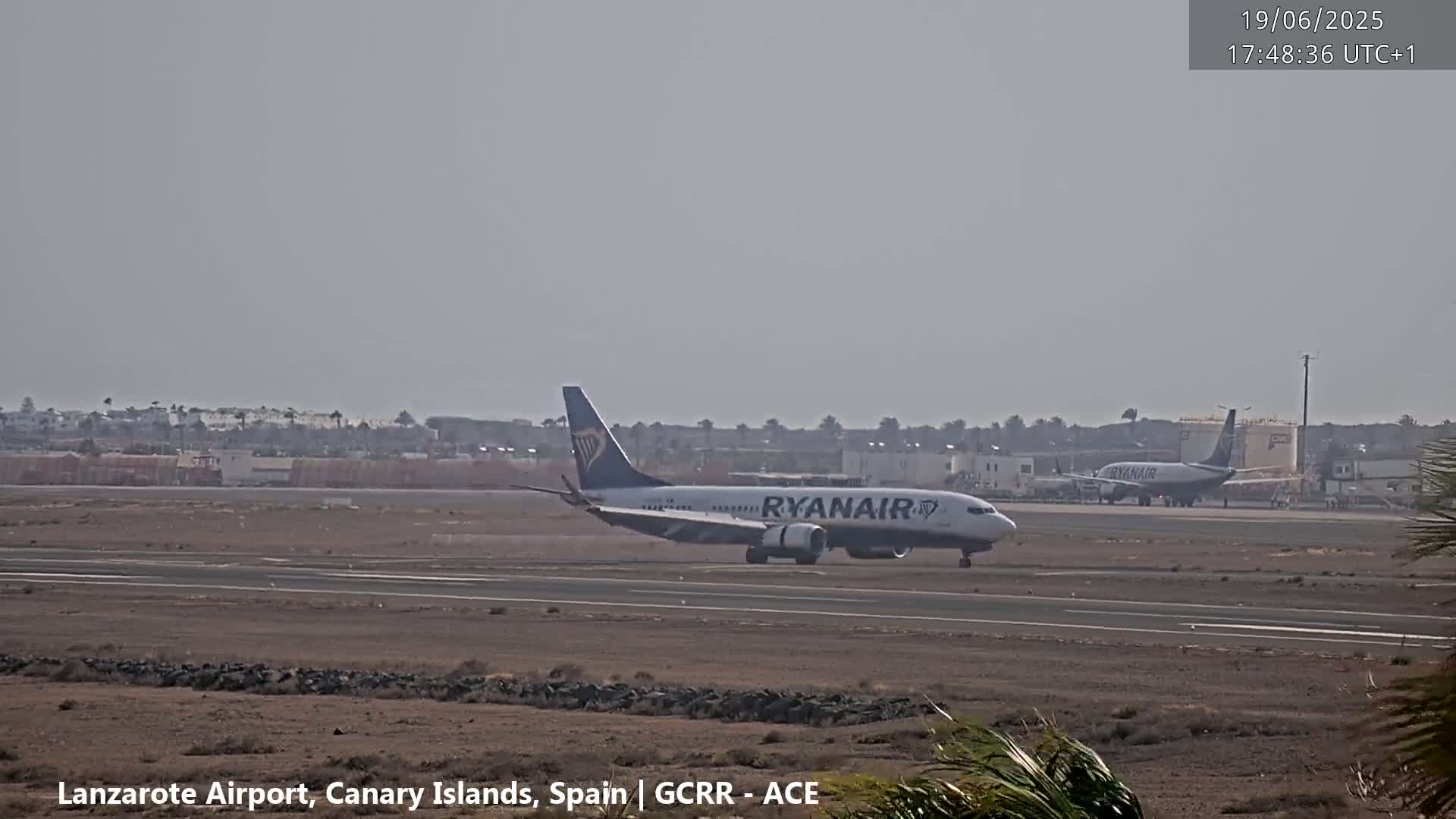 A Ryanair Boeing 737 taxis on a runway at an airport under hazy conditions.