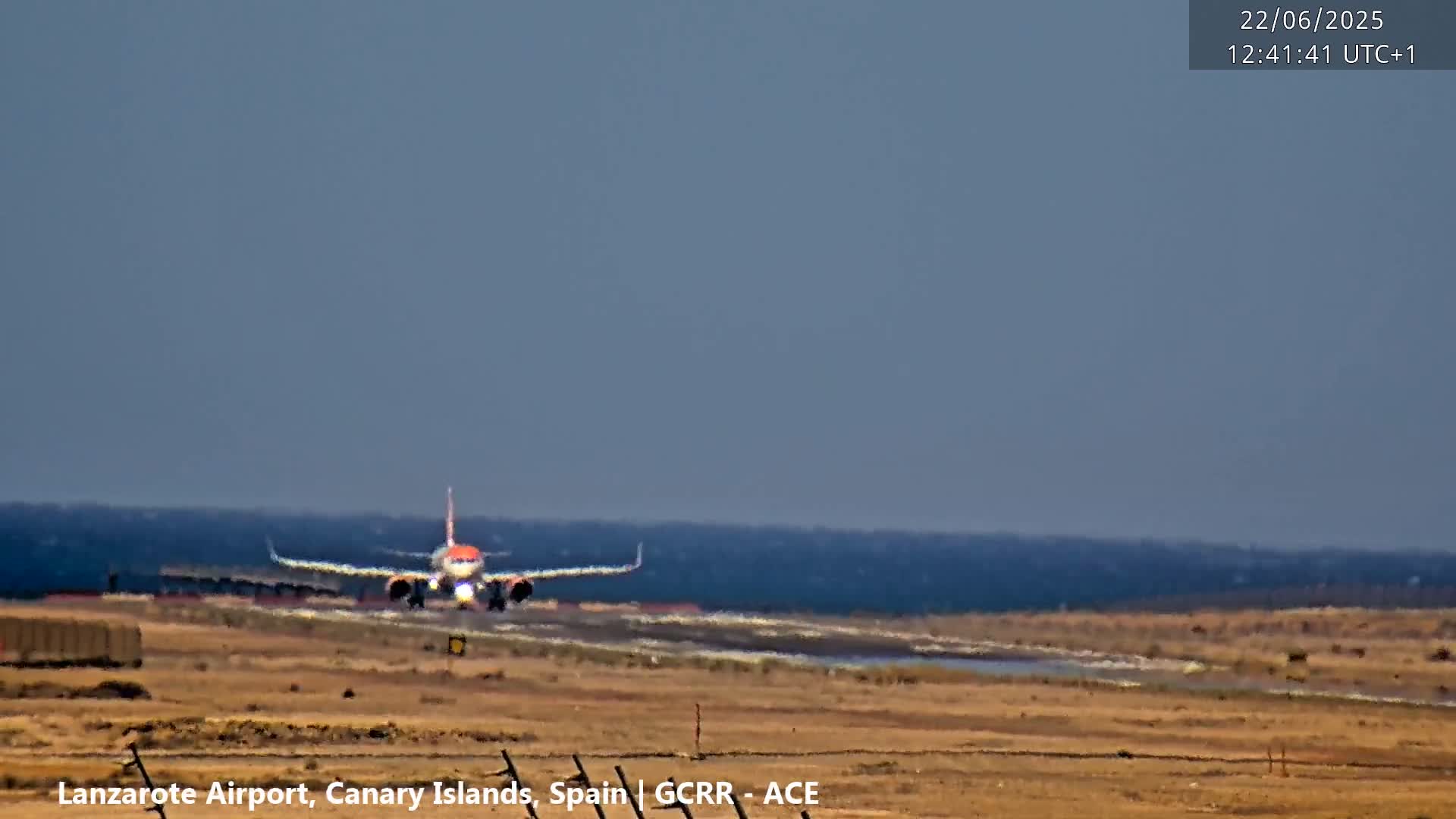 A passenger airplane is landing on a runway near a body of water under a clear sky.