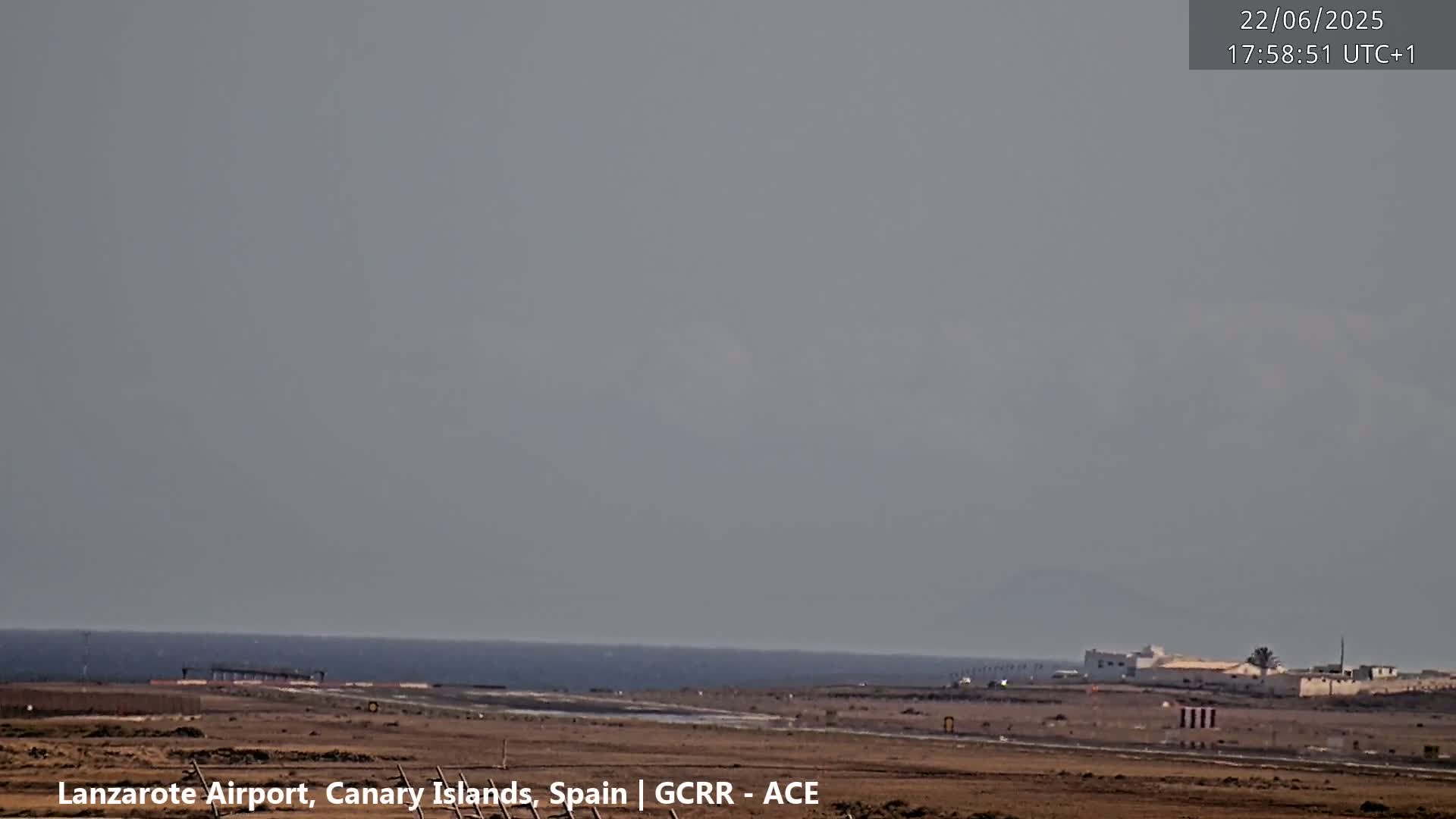 A hazy, overcast sky over a coastal airport runway with a calm ocean in the background.