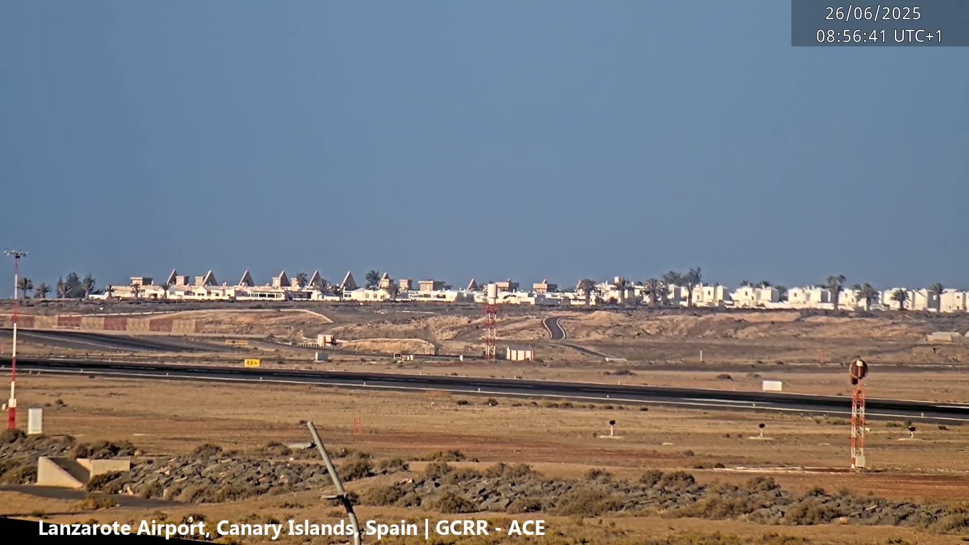 A row of low-rise buildings is visible in the distance, under a clear blue sky, from an airport runway.
