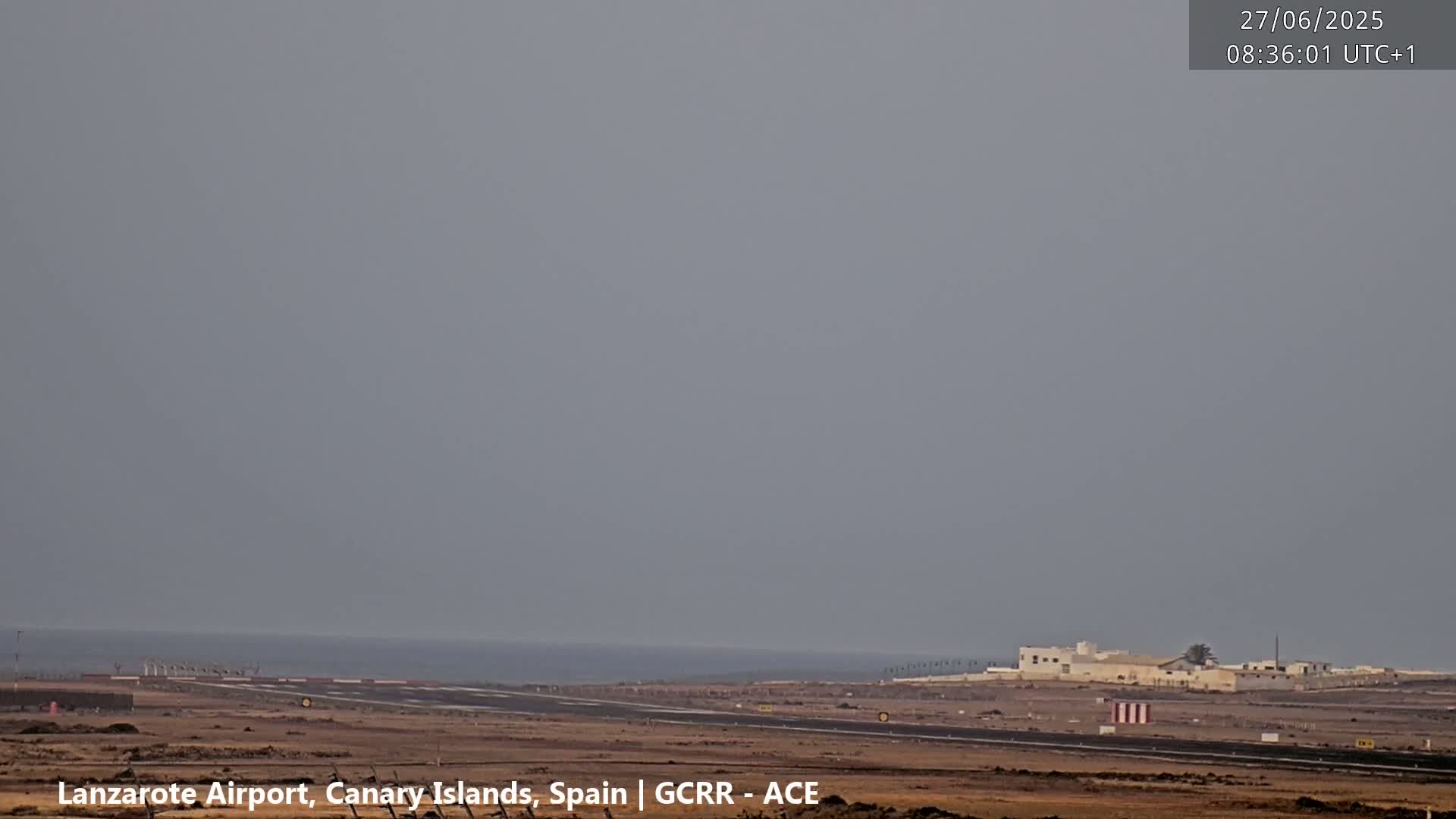A hazy, overcast sky overlooks a desolate airport runway next to a calm ocean.