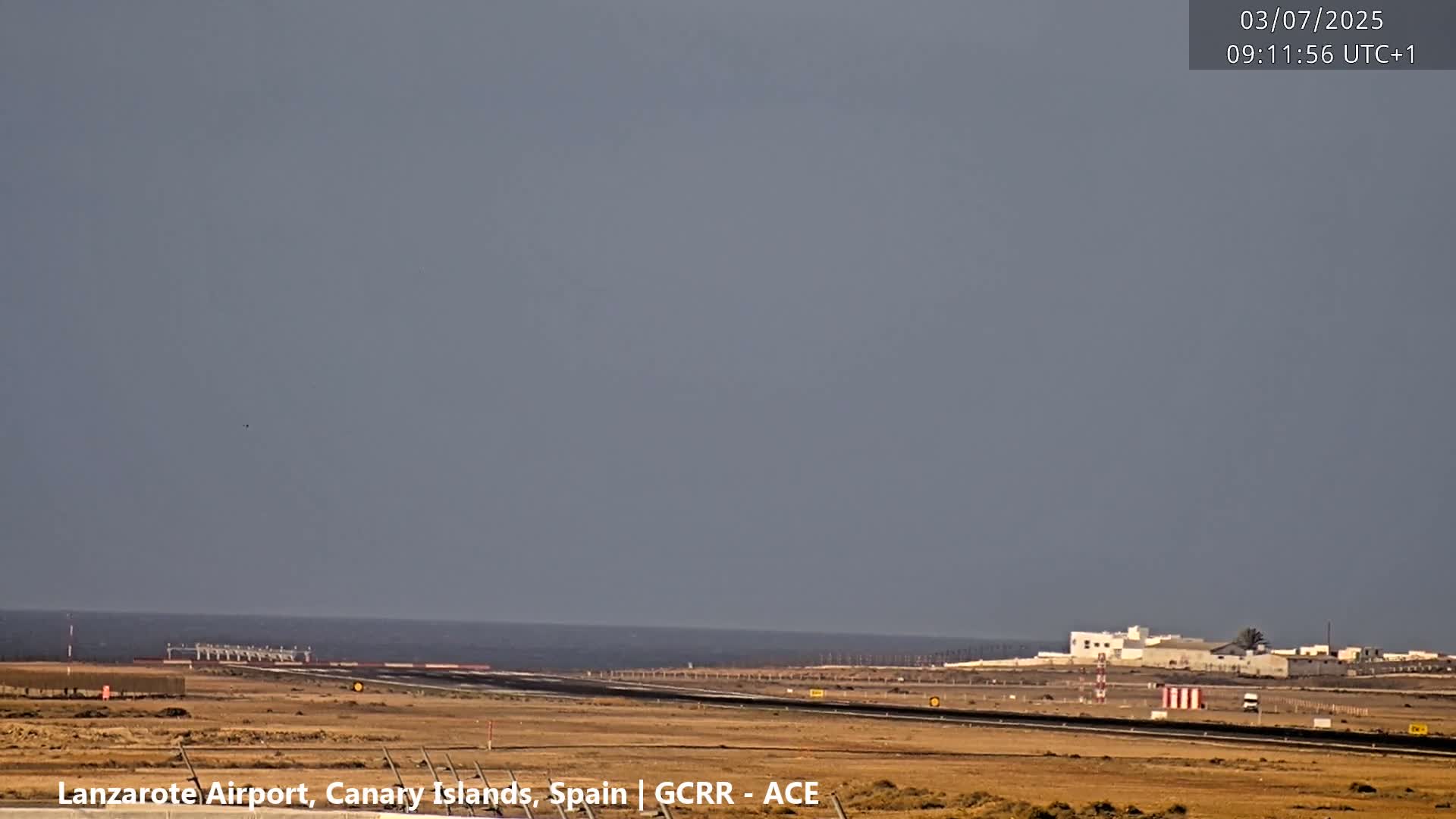 An airport runway stretches toward a calm ocean under a hazy sky.