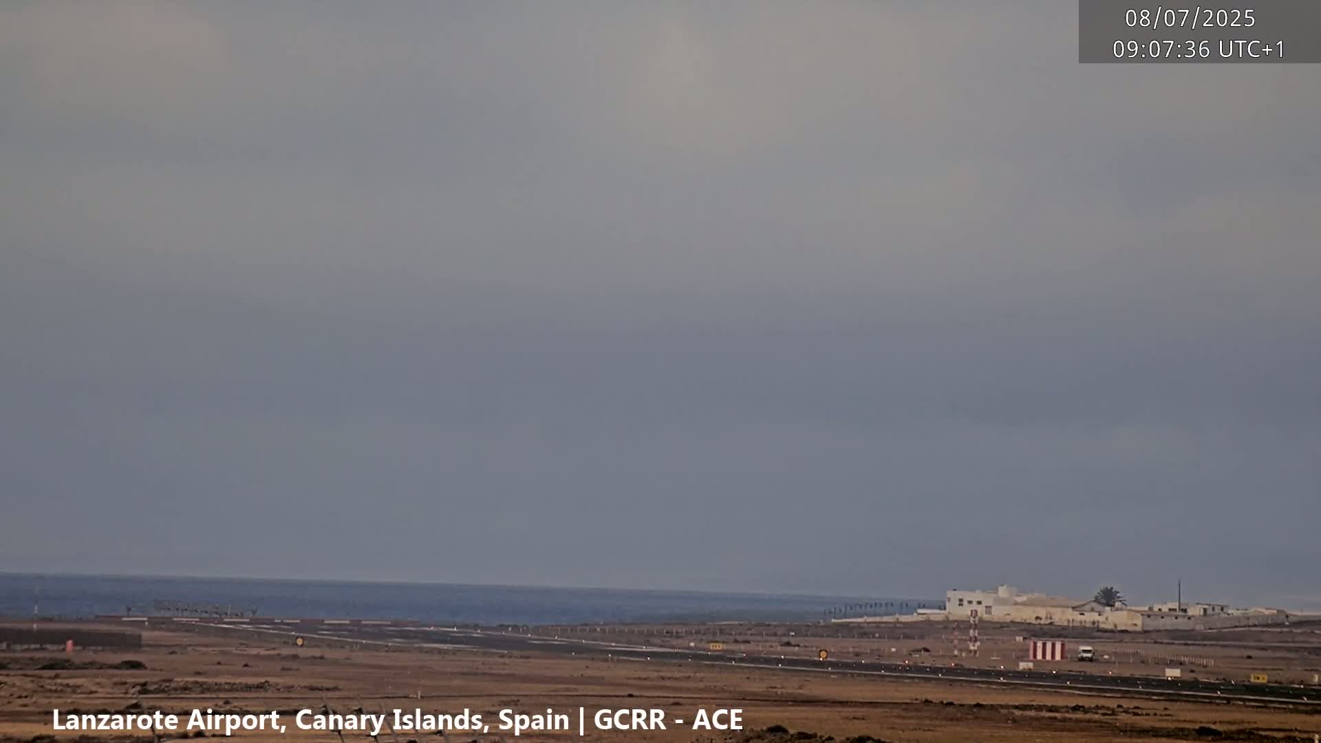 An airport runway and terminal buildings are visible near a calm ocean under an overcast sky.