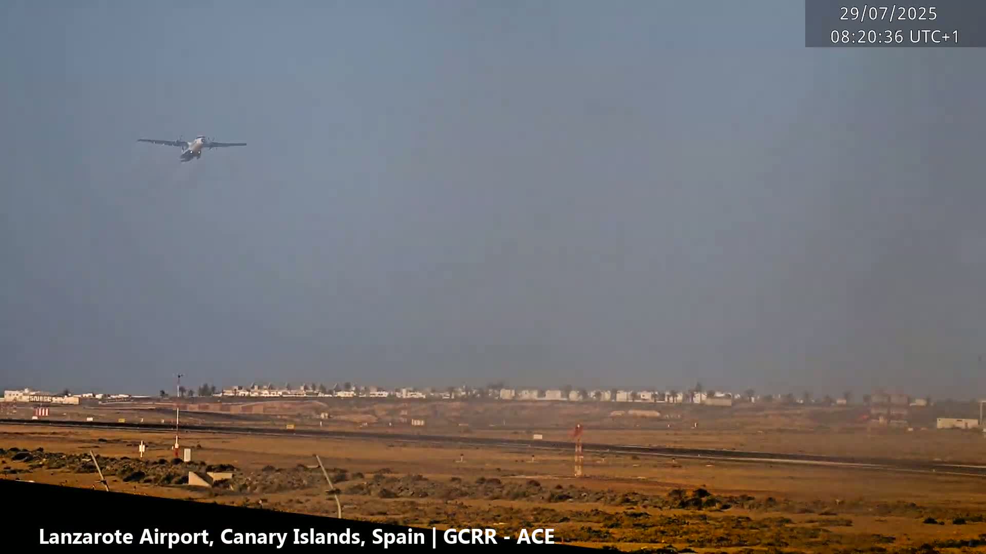 A turboprop airplane ascends over a hazy airport runway.