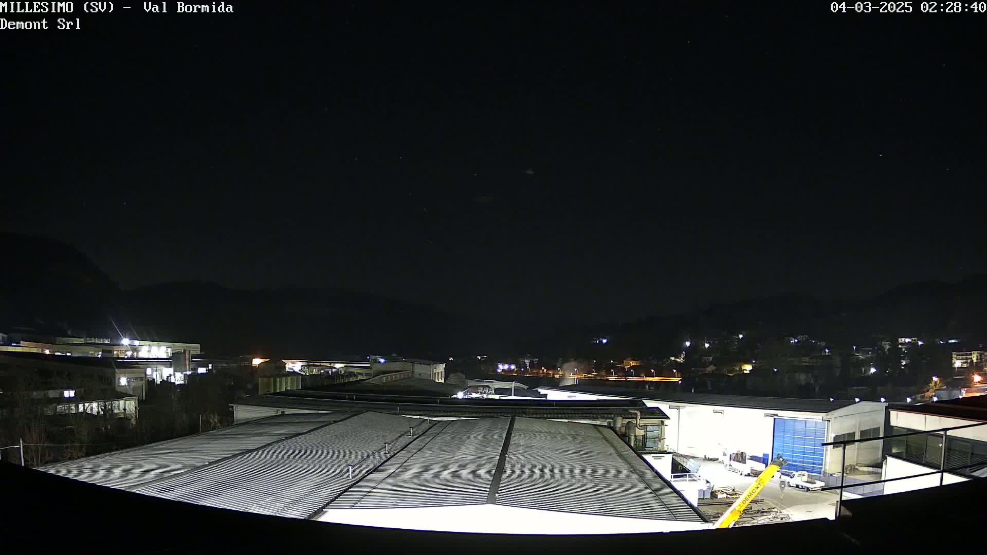 A nighttime view of industrial buildings and a town nestled in a valley under a clear, starry sky.