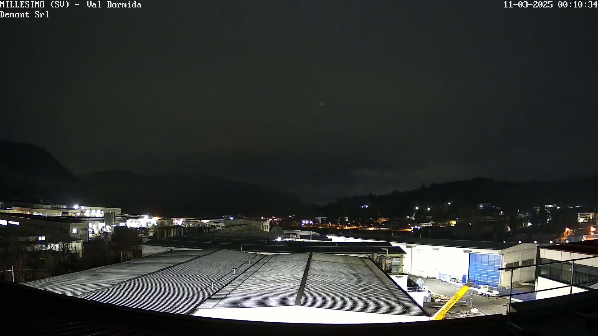 A nighttime view of an industrial area, nestled between hills under a dark, overcast sky.