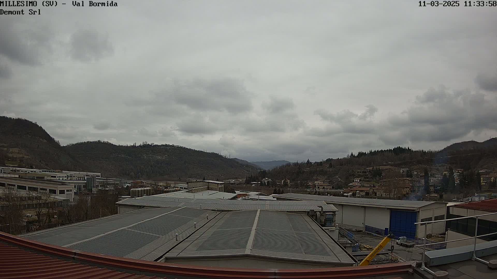 A view from a rooftop shows a cloudy day over an industrial area nestled in a valley between hills.