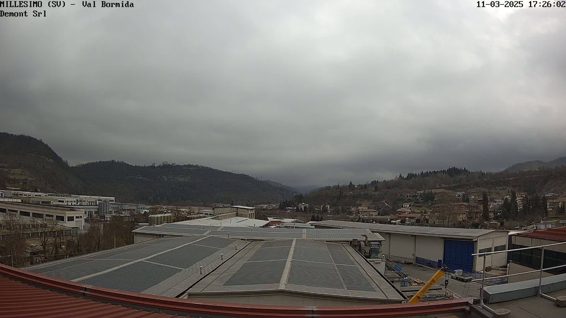 A view of an industrial area nestled in a valley between hills under an overcast sky.